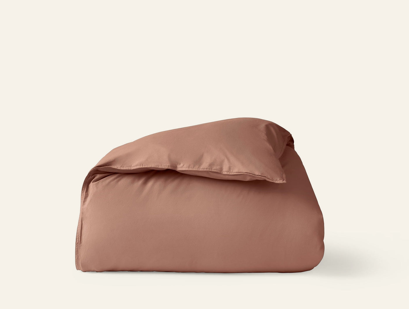 Coyuchi Crinkled Percale duvet cover in terracotta, folded with pillow on white background.