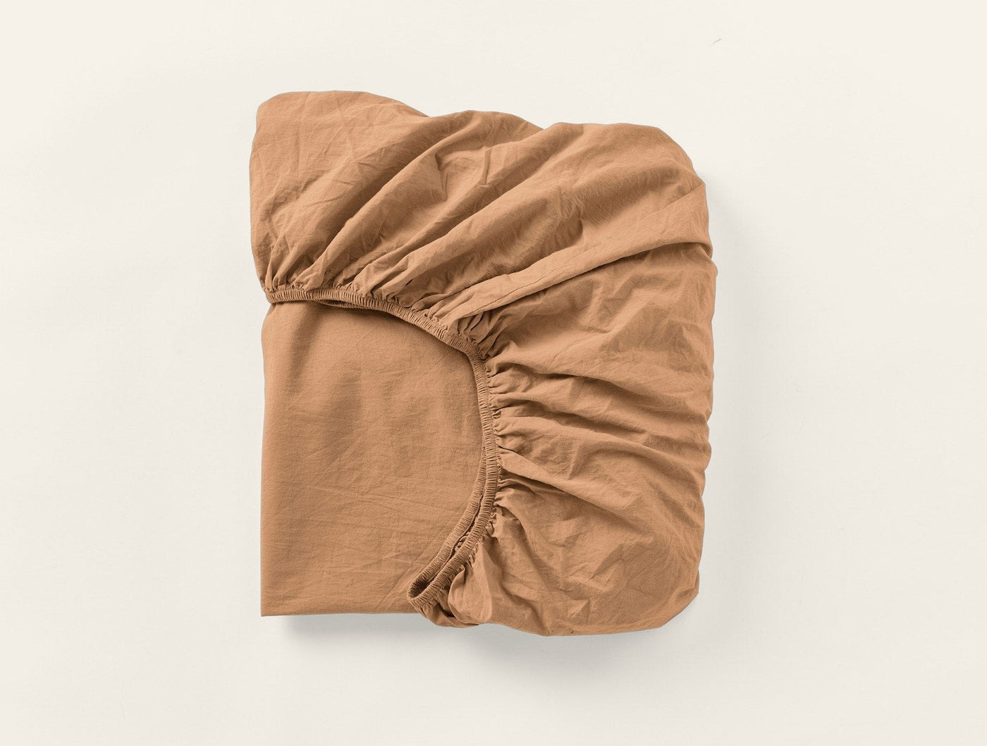 Coyuchi Crinkled Percale fitted sheet in caramel, folded to show elasticated corners.