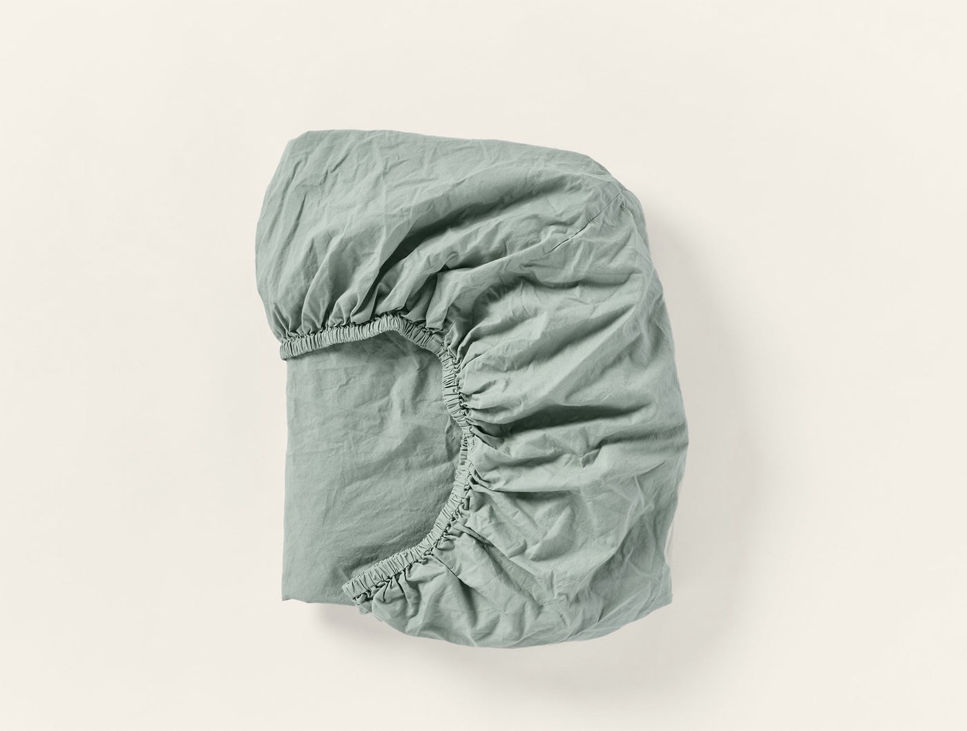 Sage green fitted sheet folded to show elasticized corner, crinkled percale texture visible.