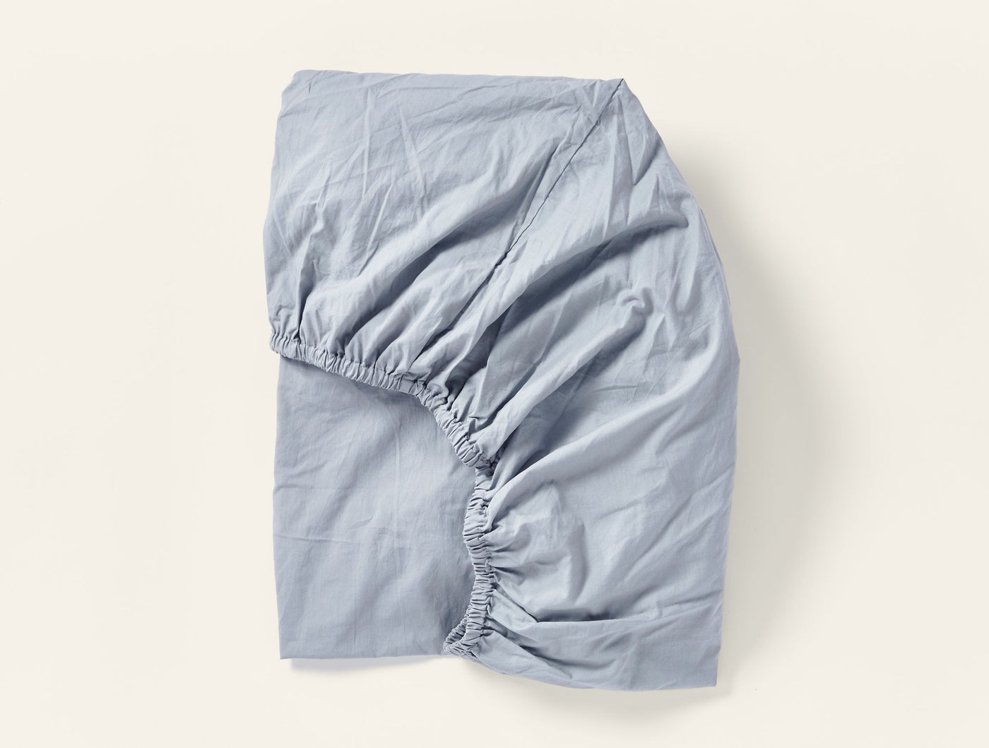 Slate blue fitted sheet folded to show elasticated corners and crinkled percale texture.