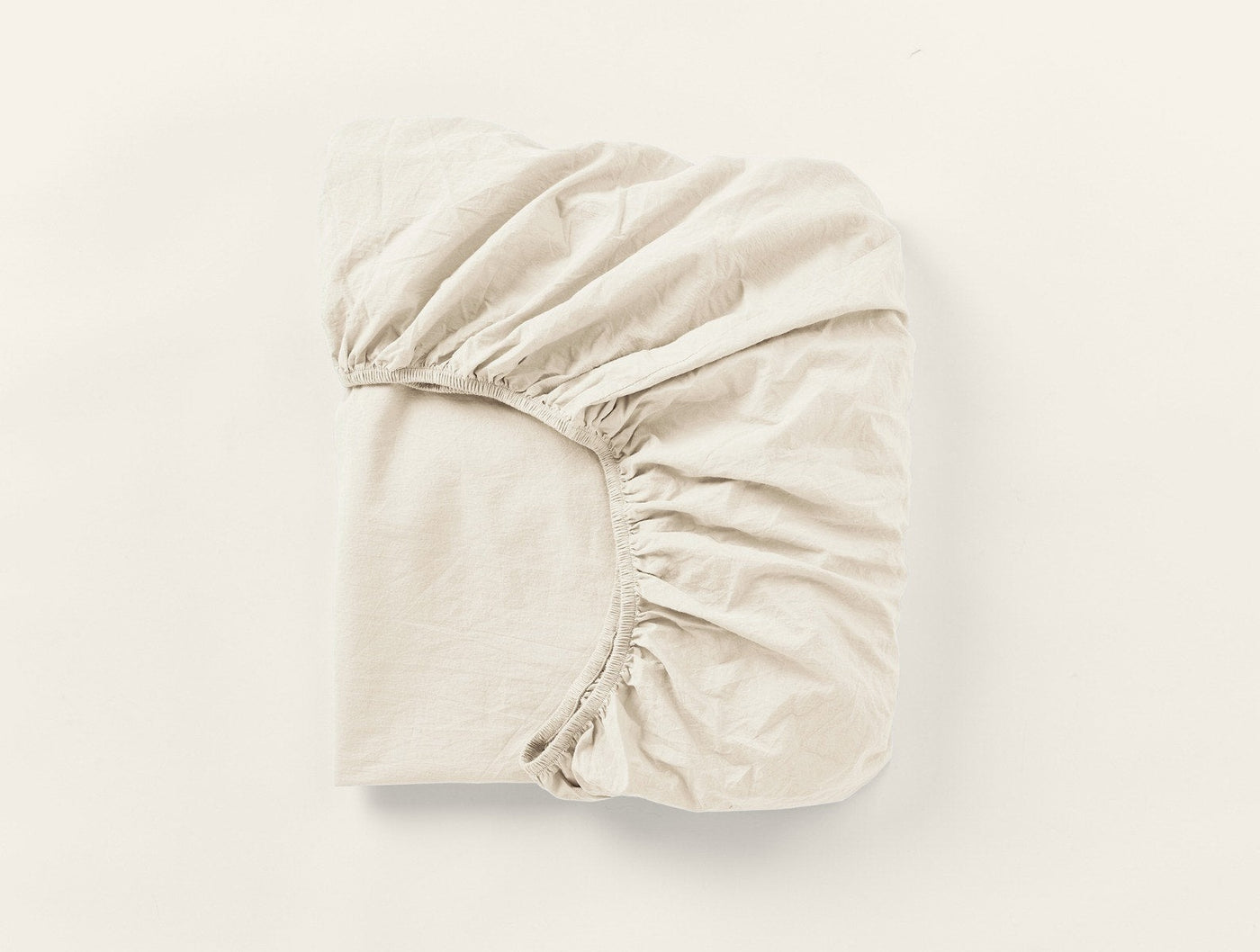 Folded ivory fitted sheet showing elasticized corners and crinkled percale texture.