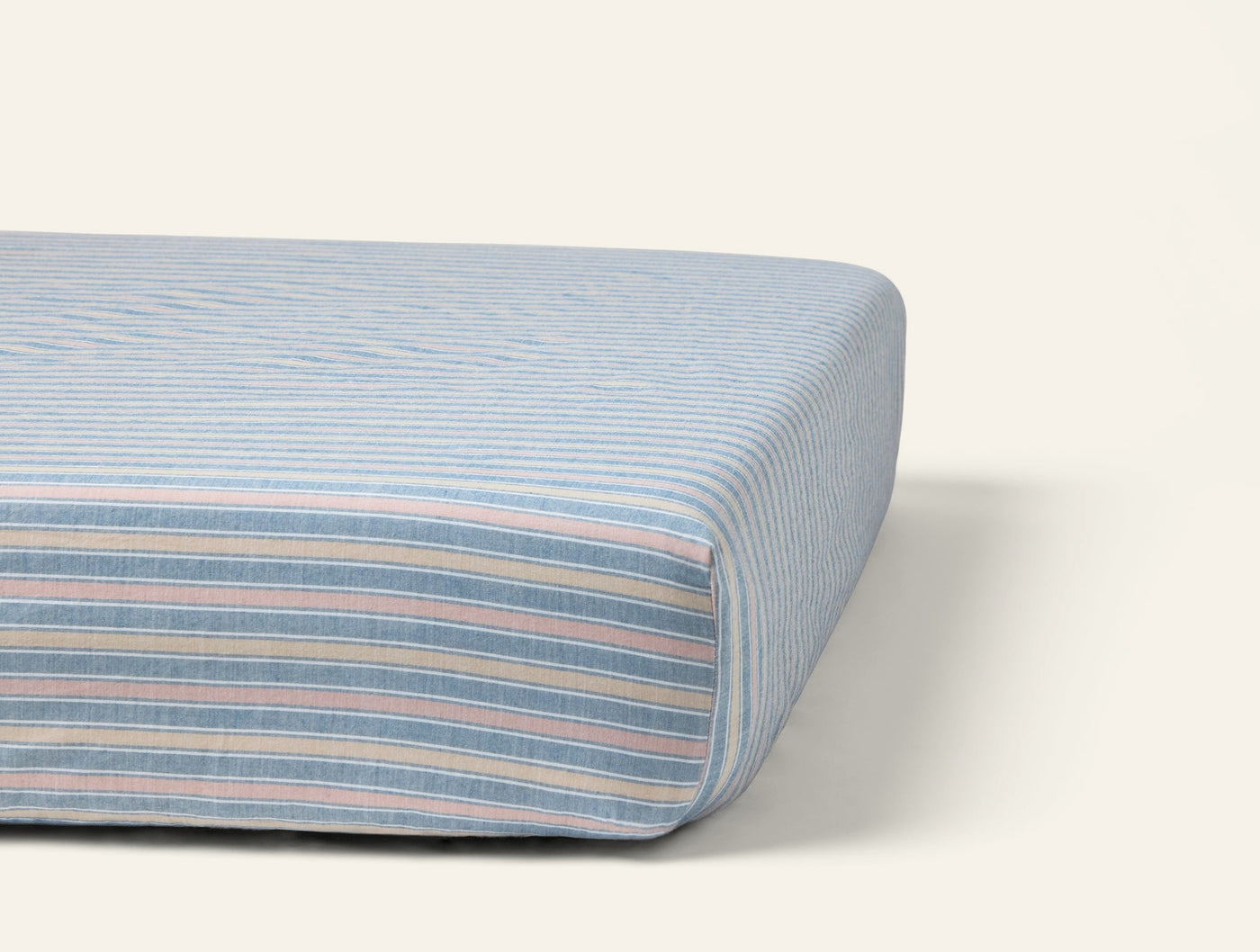 Corner detail of Coyuchi Crinkled Percale fitted sheet in multicolor pastel stripes on a mattress.
