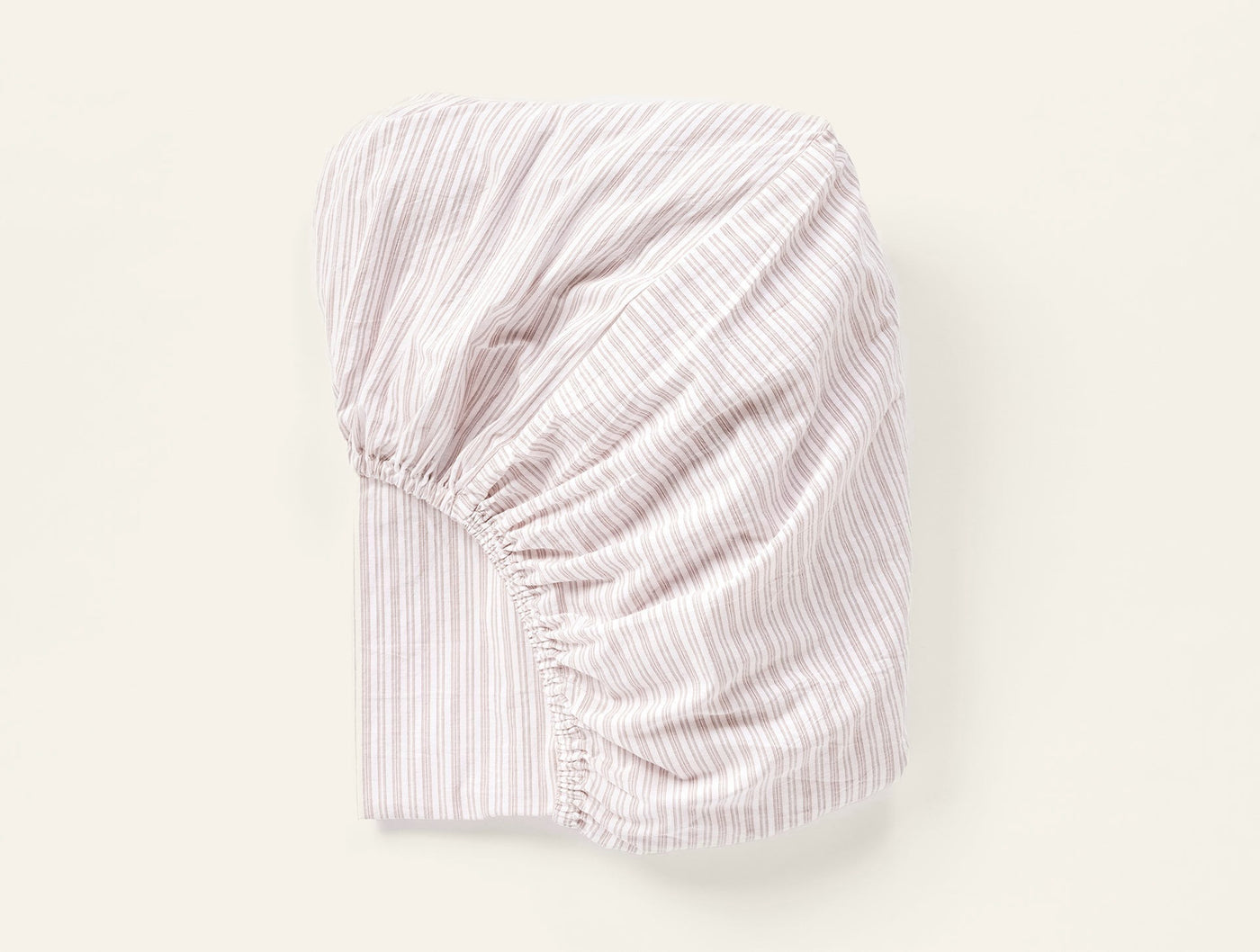 Elasticized corner detail of a blush and white striped crinkled percale fitted sheet, folded.
