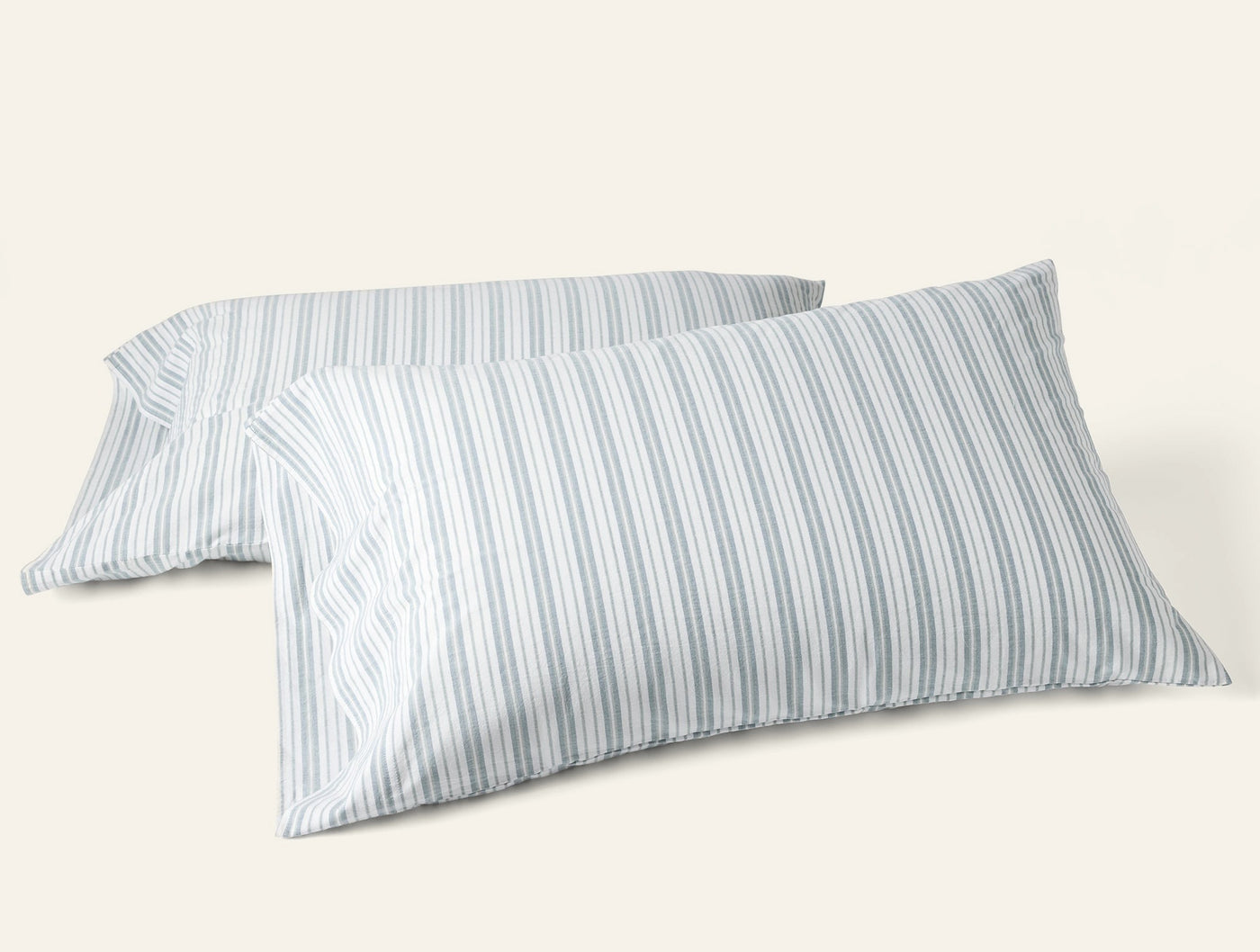 Two Coyuchi Crinkled Percale pillowcases in soft blue-grey ticking stripes, stacked at an angle.