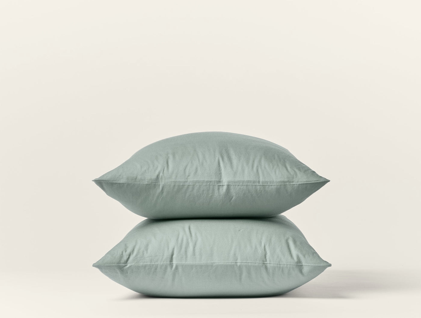 Two stacked sage Coyuchi Crinkled Percale pillowcases with subtle texture against white background.