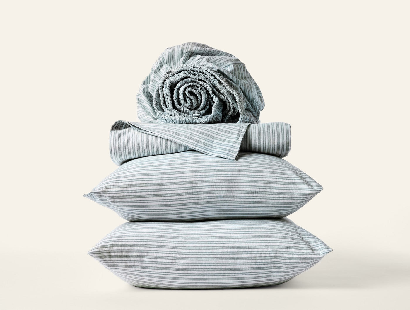 Coyuchi Crinkled Percale pillowcases stacked with striped sheets rolled on top.