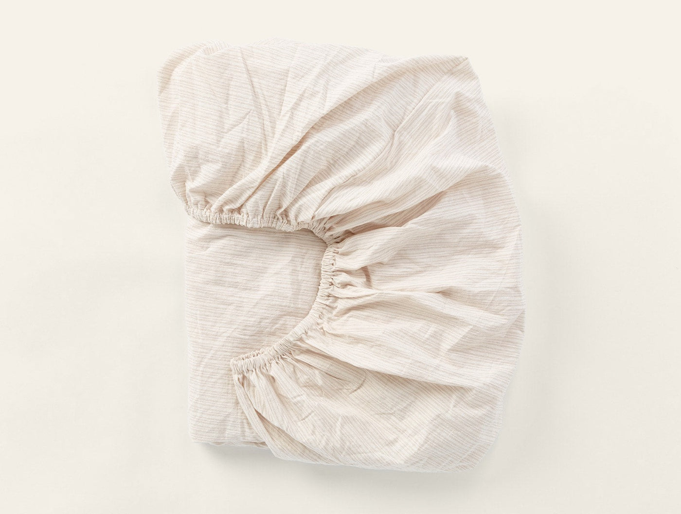 Fitted sheet in ivory crinkled percale, elasticated corners visible, folded flat.