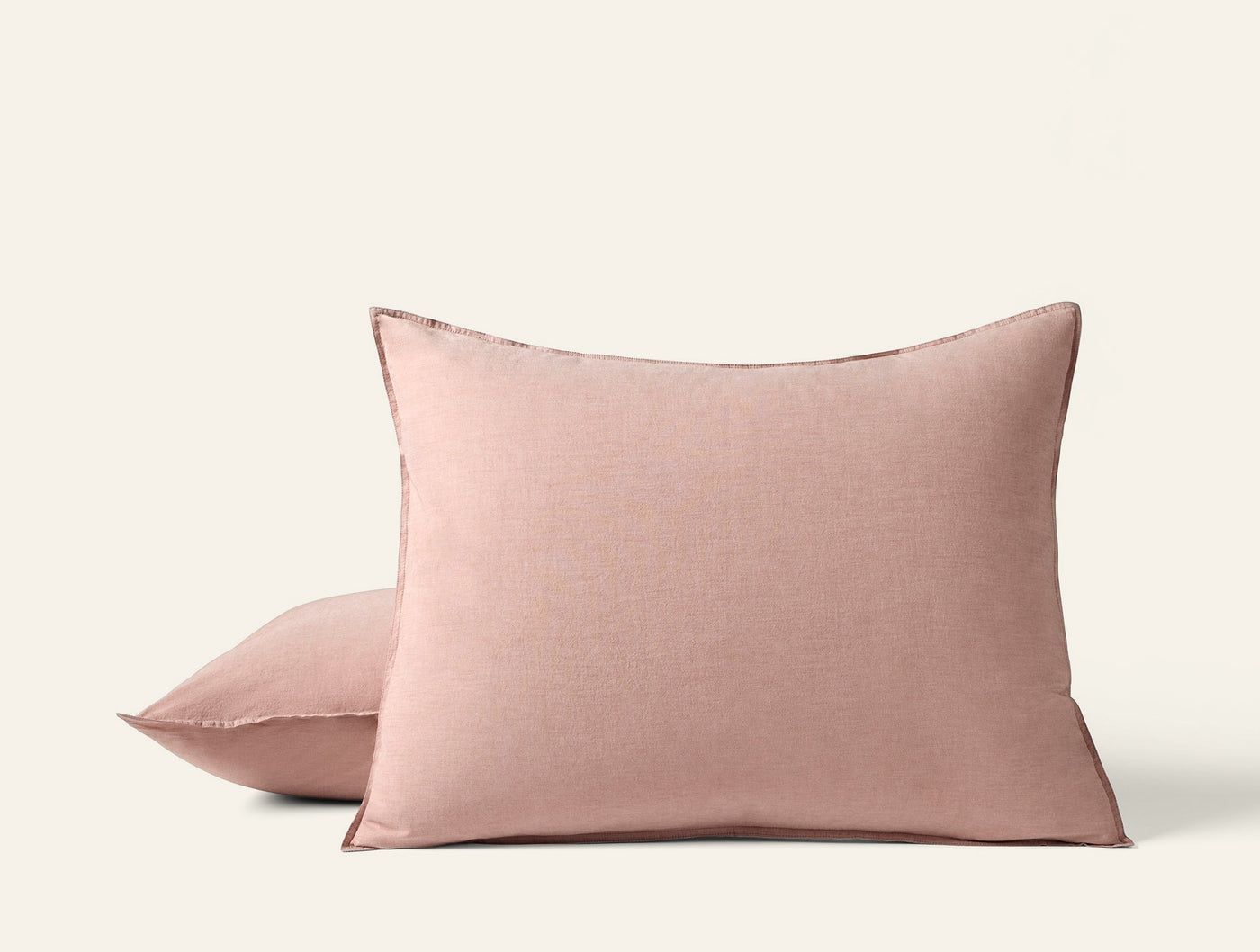 Close-up of two blush Coyuchi Crinkled Percale pillow shams stacked on white background.
