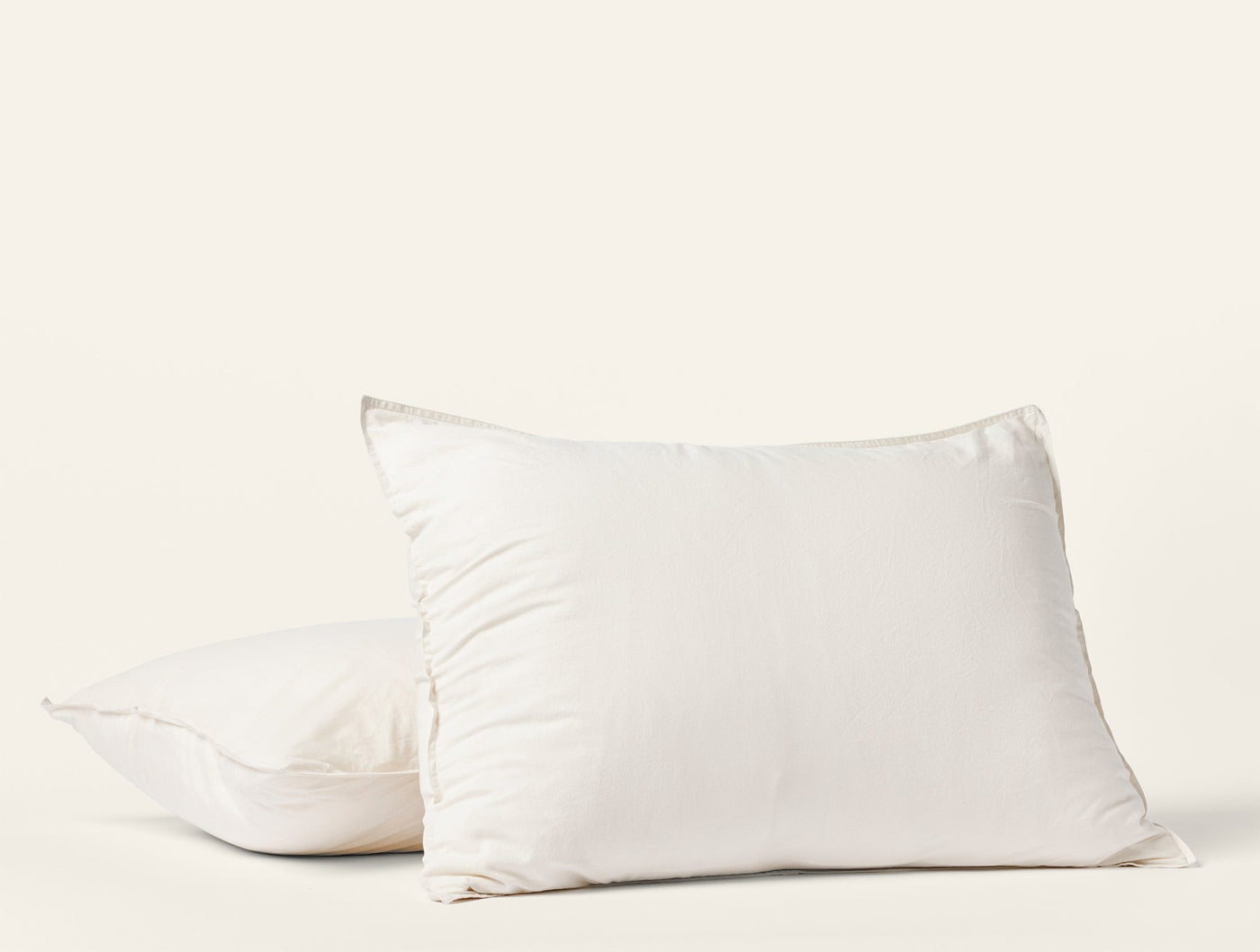 Close-up of two ivory Coyuchi Crinkled Percale pillow shams stacked against white background.