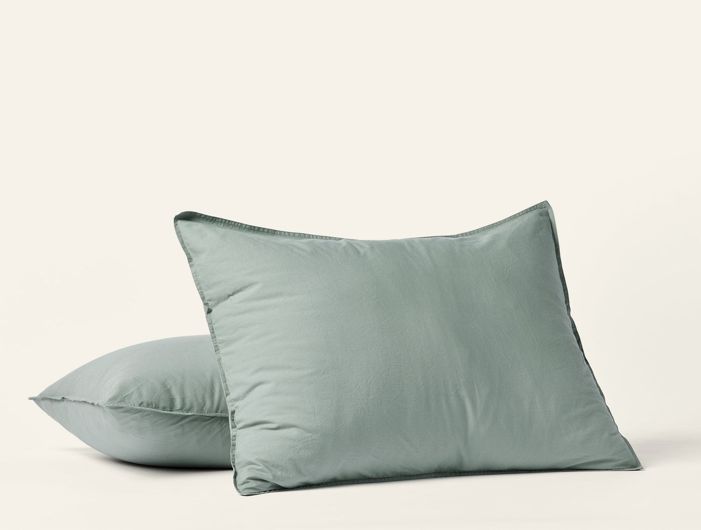 Close-up of two sage Coyuchi Crinkled Percale pillow shams stacked on white background.