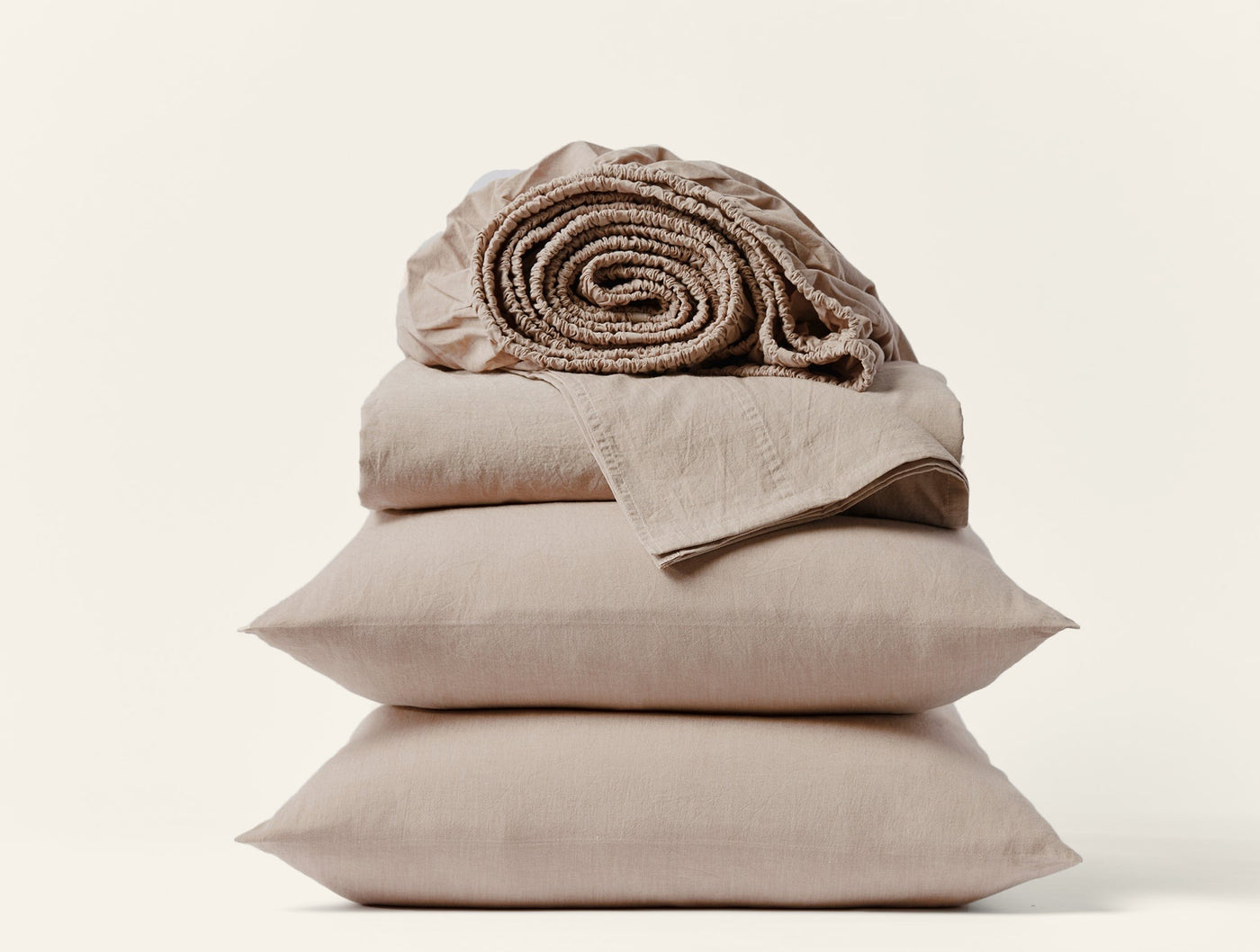 Rolled fitted sheet atop stacked flat sheet and two pillowcases in taupe crinkled percale.