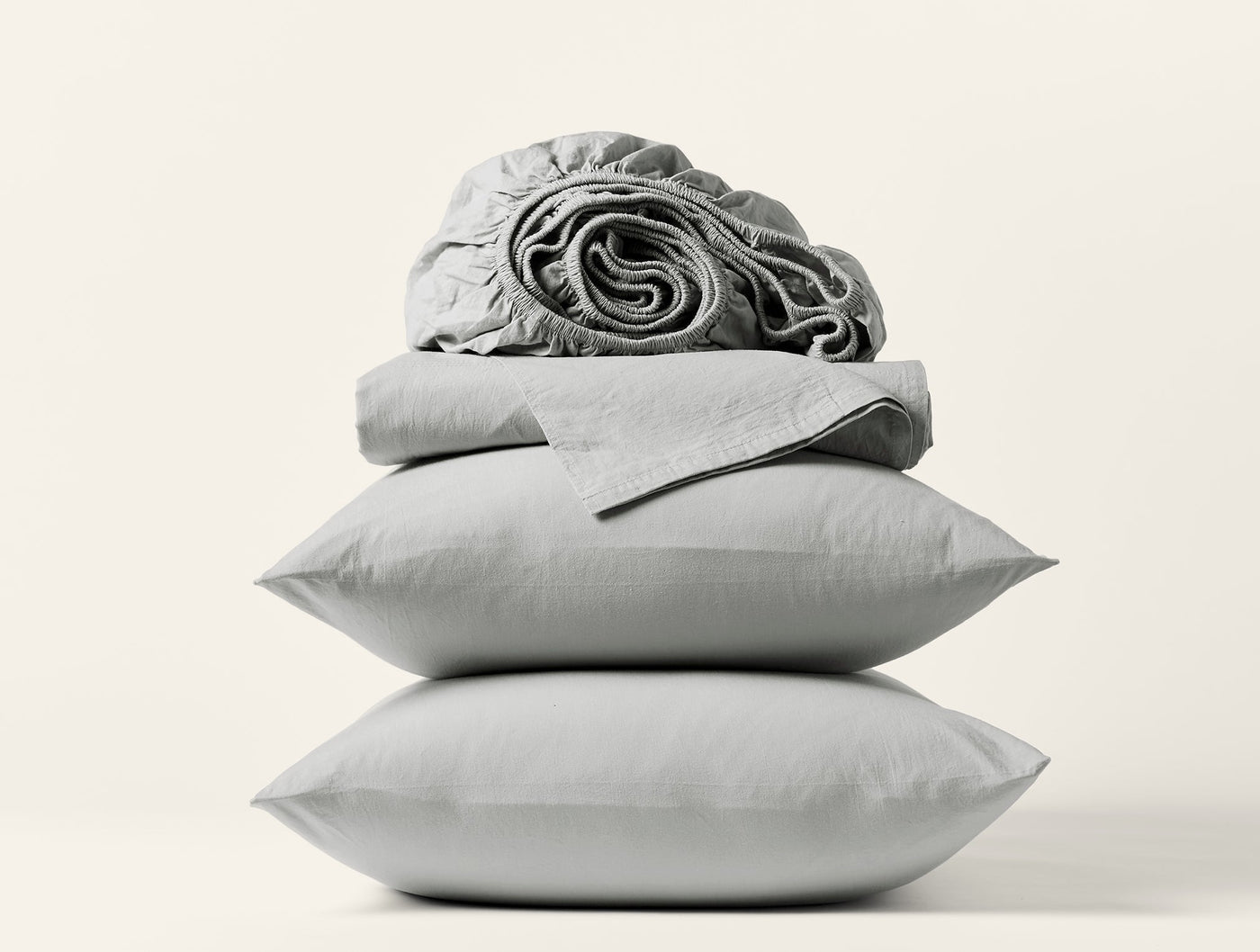 Stacked silver Coyuchi Crinkled Percale pillowcases and folded sheet set against white background.