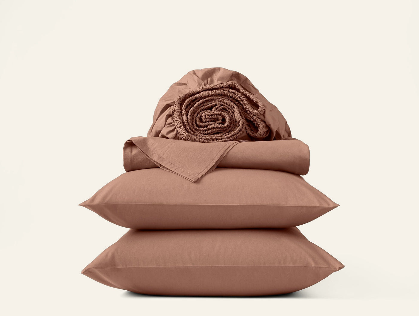Stacked Coyuchi Crinkled Percale sheet set in terracotta, folded flat sheets and two pillowcases with rolled fitted sheet on top.