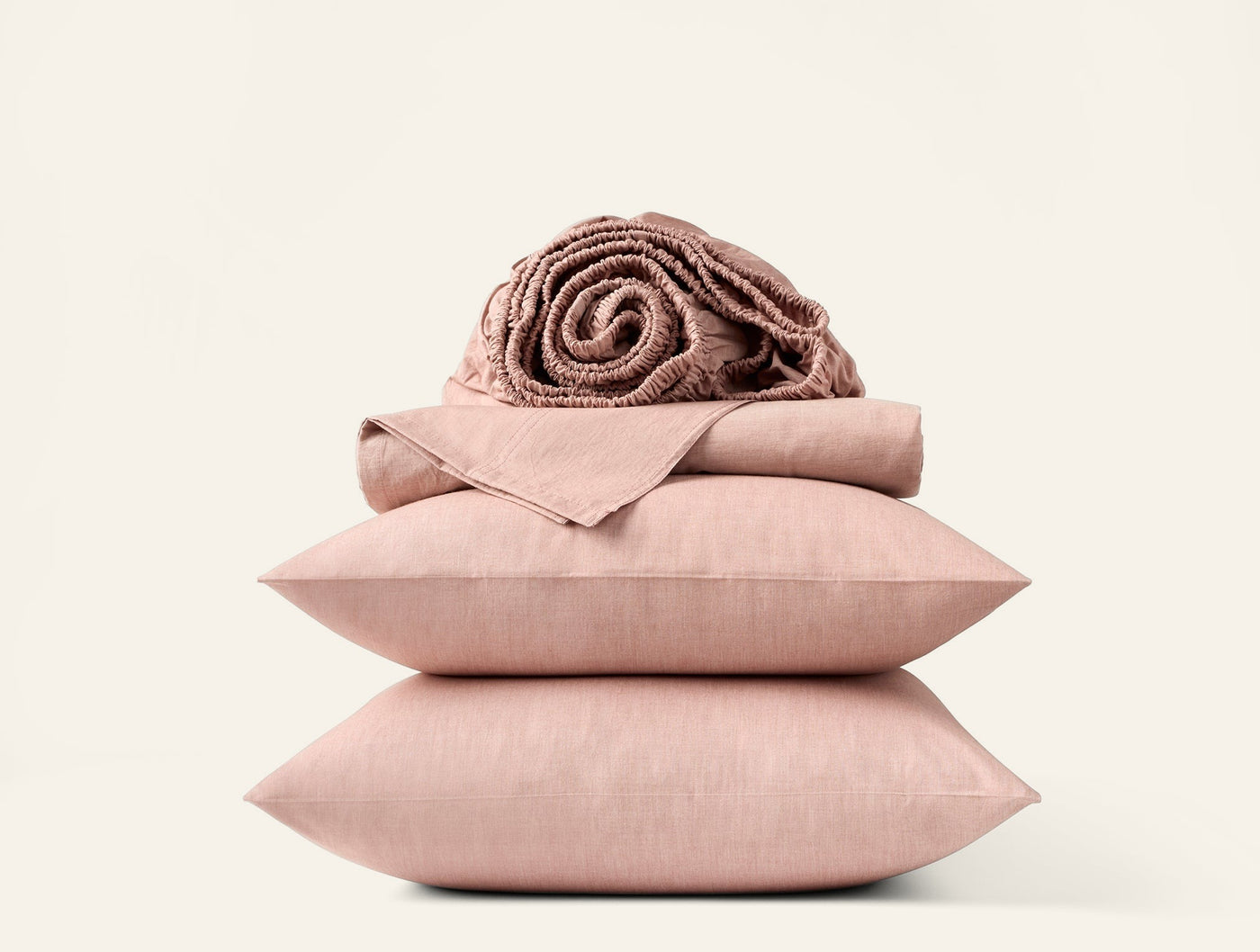 Blush pink crinkled percale sheet set folded and stacked with matching pillows and a rolled blanket.