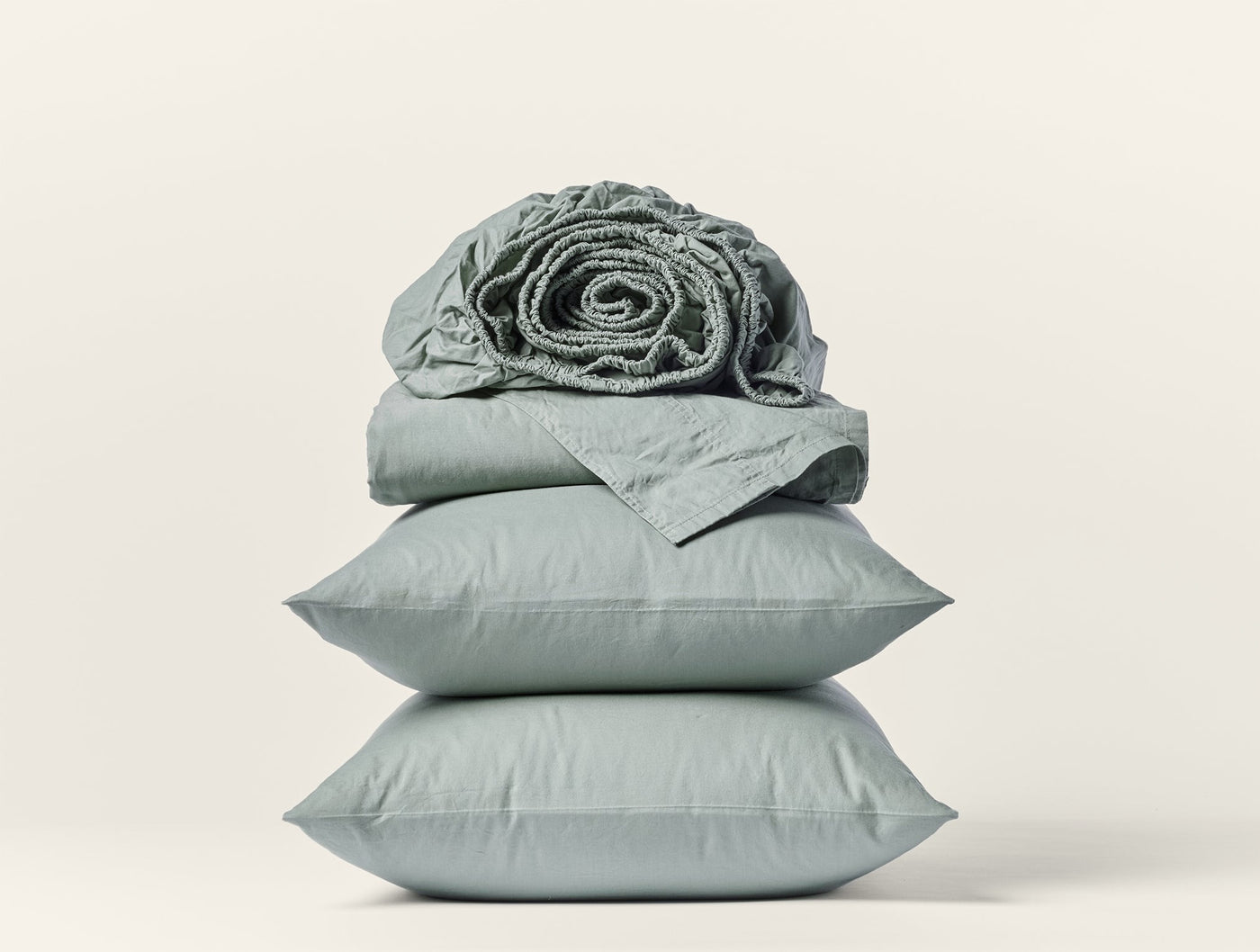 Sage green Coyuchi Crinkled Percale sheet set stacked with rolled fitted sheet on top.