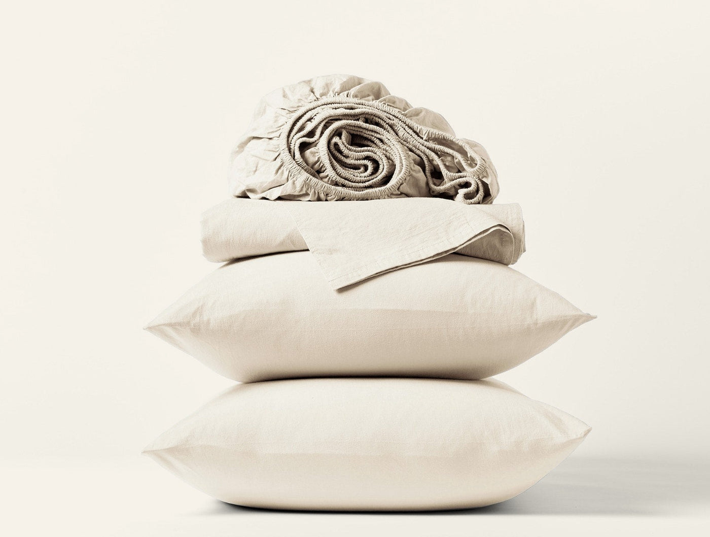 Rolled and folded ivory crinkled percale sheets stacked atop two pillowcases on white background.