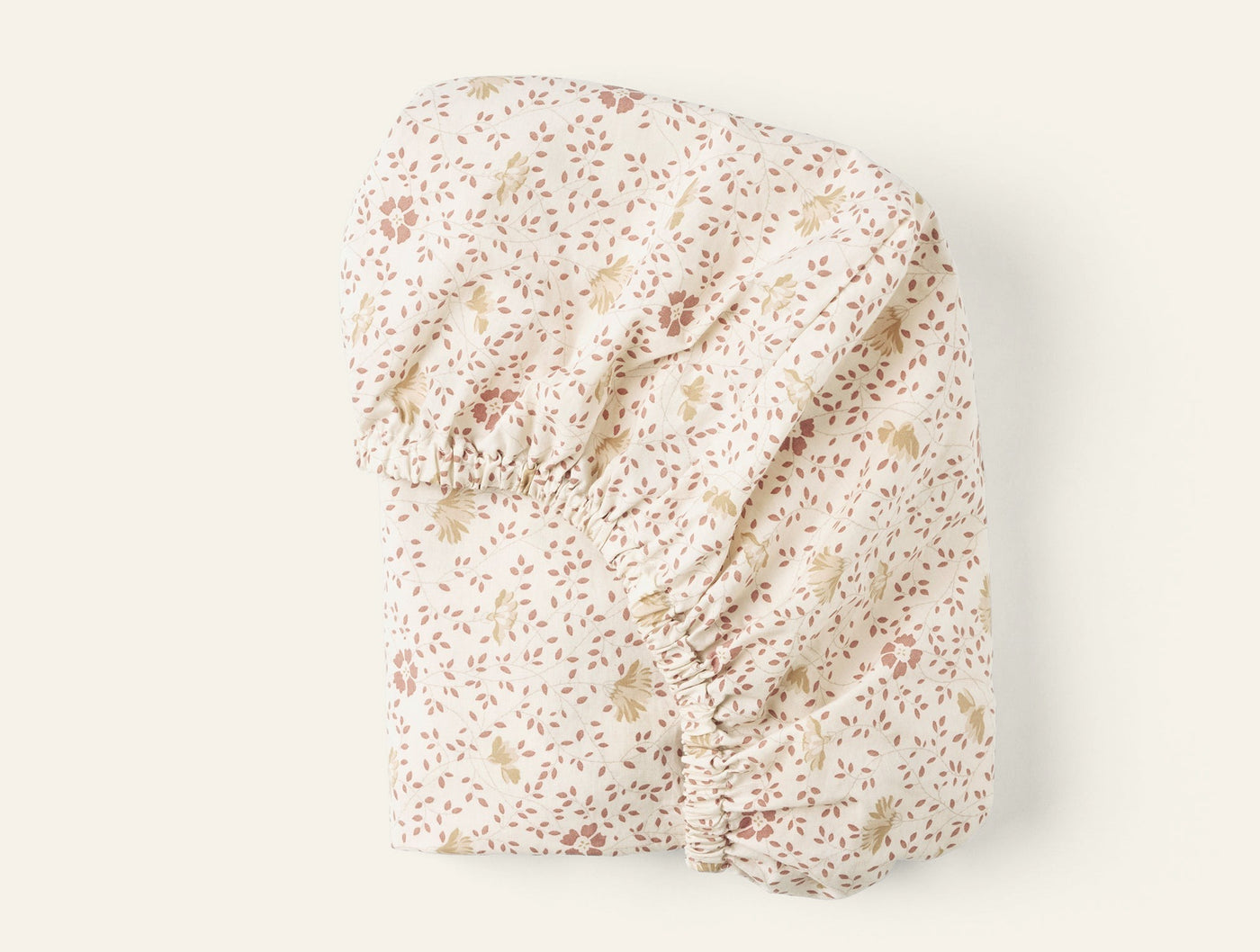 Folded ivory fitted sheet with delicate pink and gold floral print, elastic ruching visible.