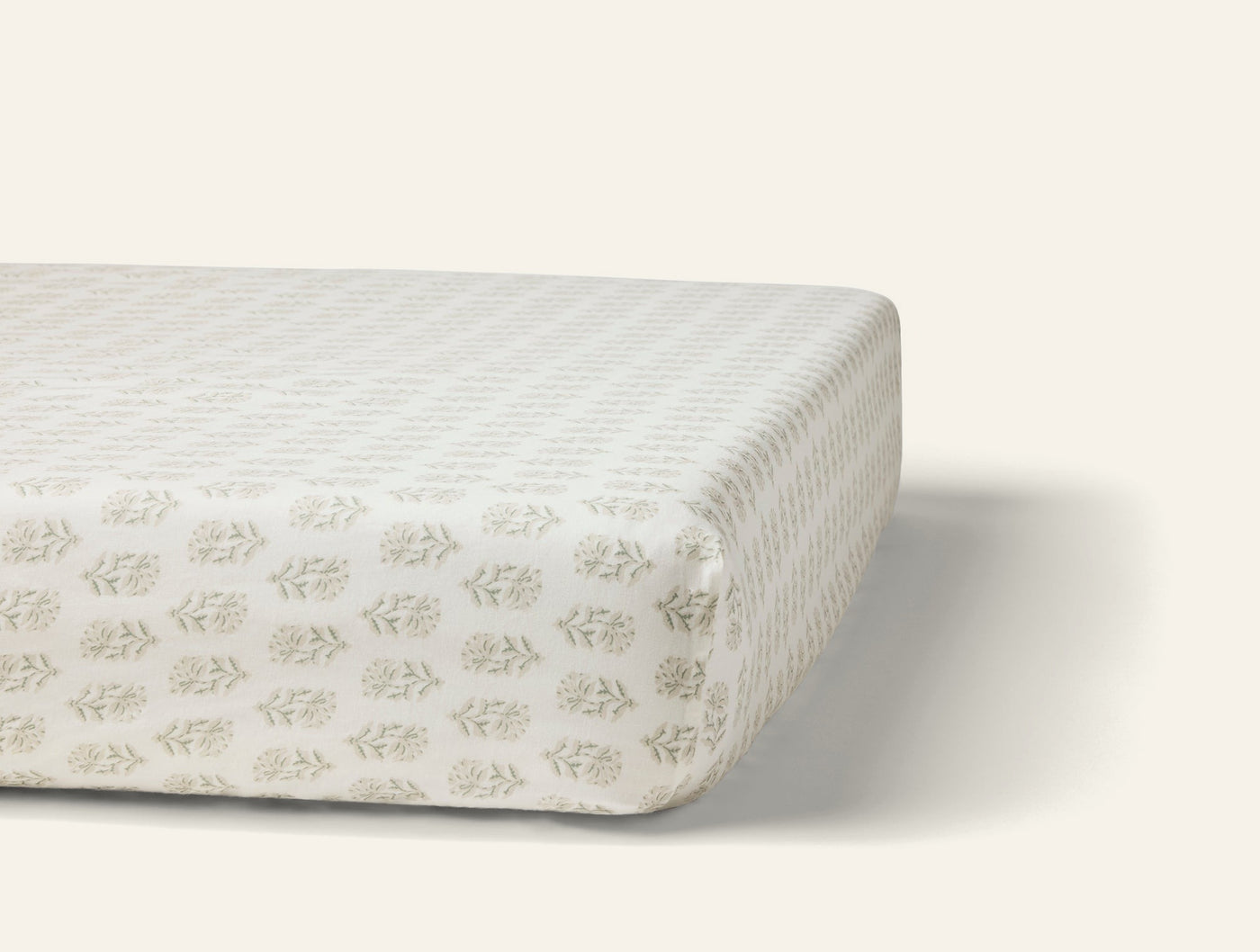 Angled view of fitted sheet on mattress, sage block-print botanical motif on ivory percale.