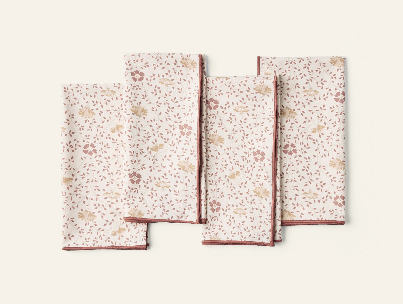 Four Coyuchi Print Percale napkins fanned flat, ivory with rose floral print and brick red trim.