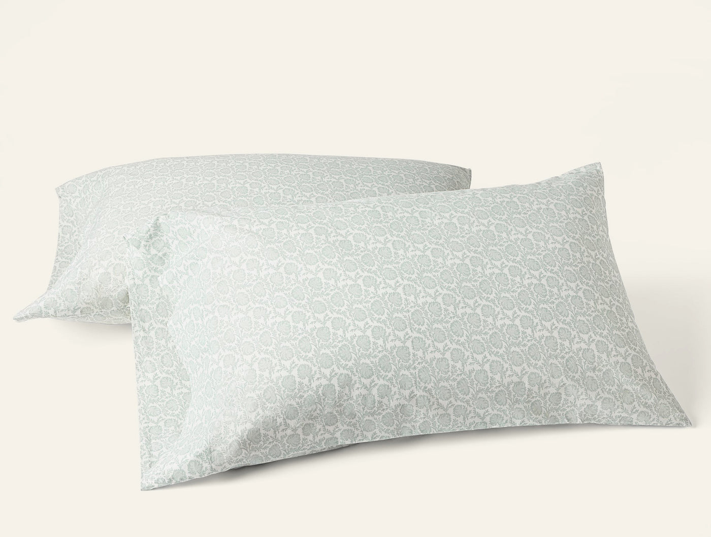 Two Coyuchi Print Percale pillowcases in sage green geometric pattern, angled view.