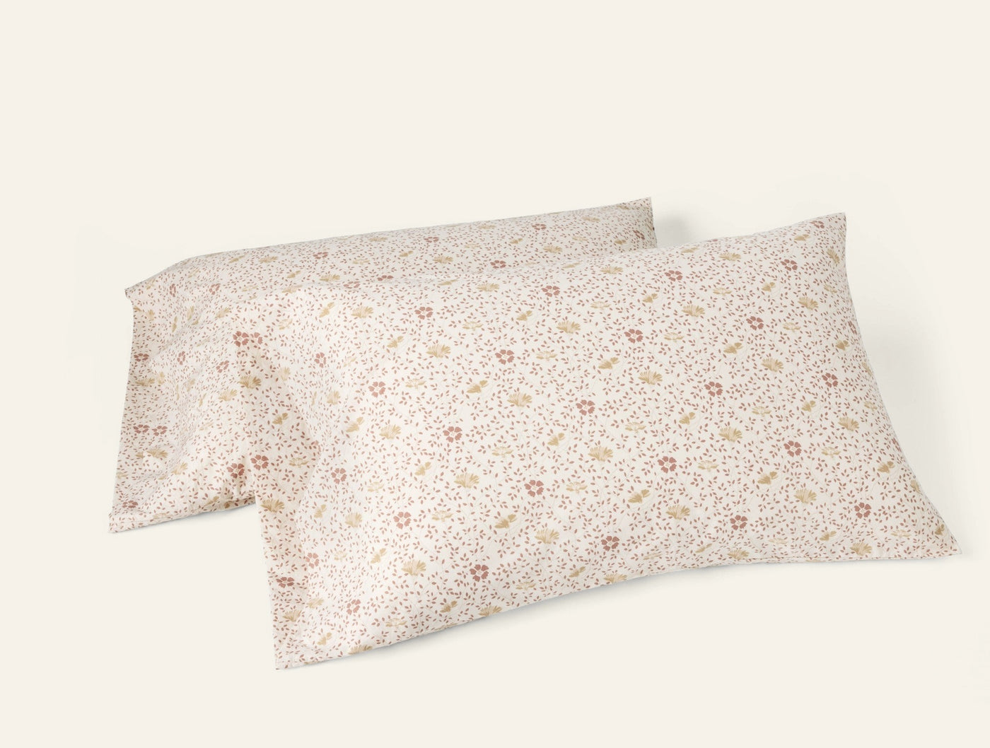 Two Coyuchi ivory percale pillowcases with small scattered ditsy floral print in blush and gold.