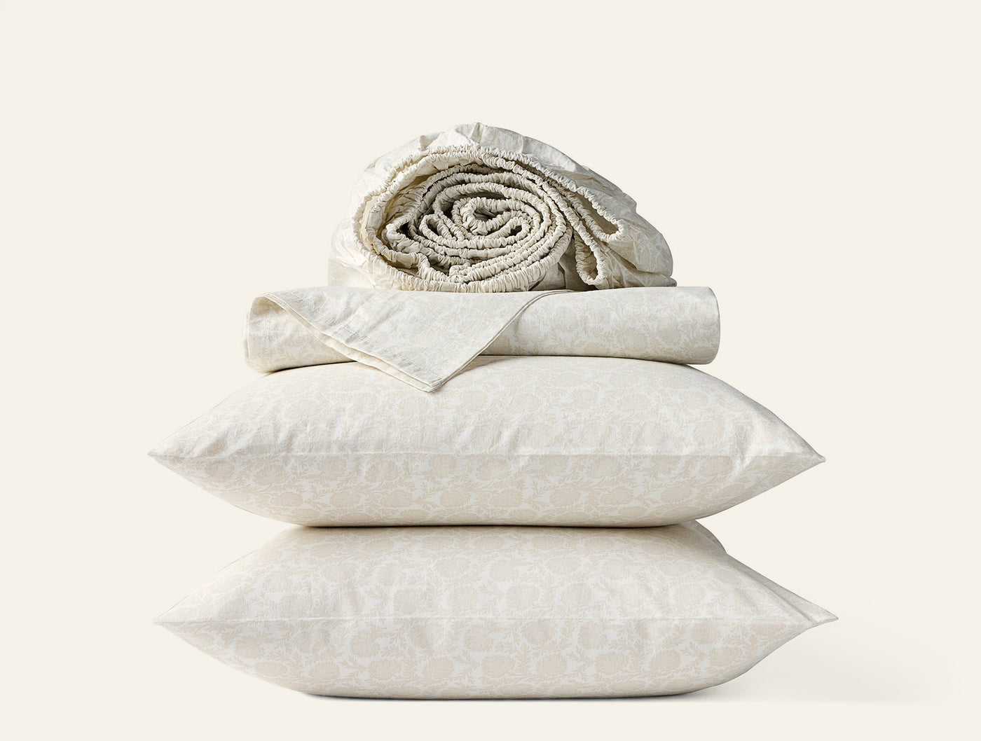 Stacked ivory percale pillowcases with subtle print, flat sheet, and rolled fitted sheet above.