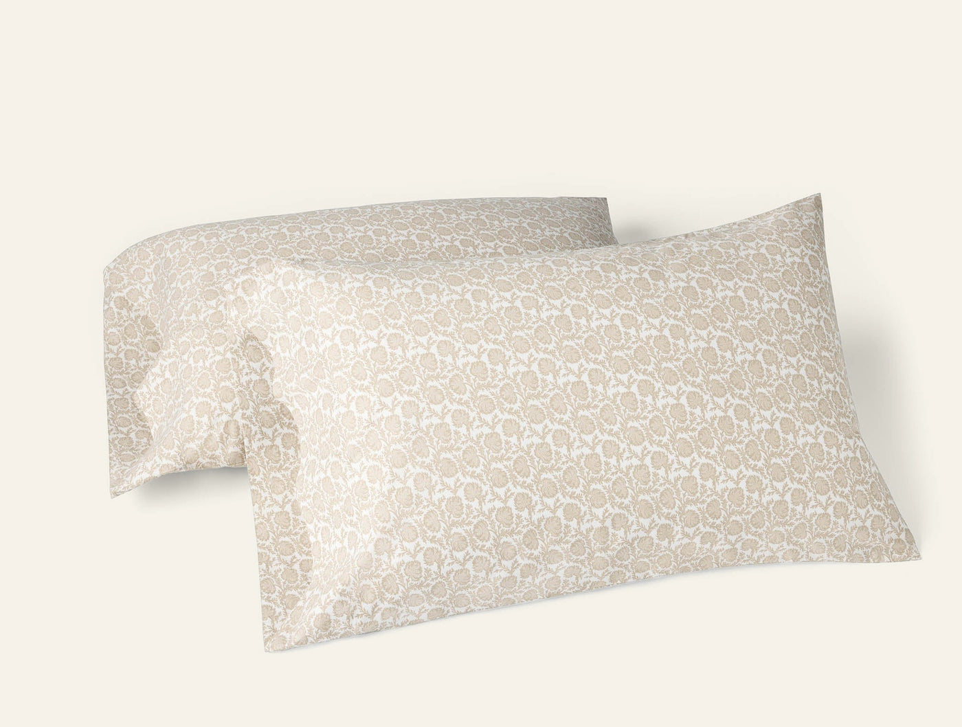 Pair of Coyuchi percale pillowcases in sand with tonal floral geo print, stacked at an angle.