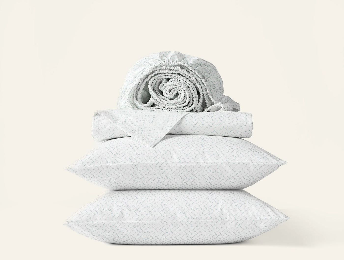 Close-up of two white Coyuchi Print Percale pillowcases stacked with folded sheets on white background.