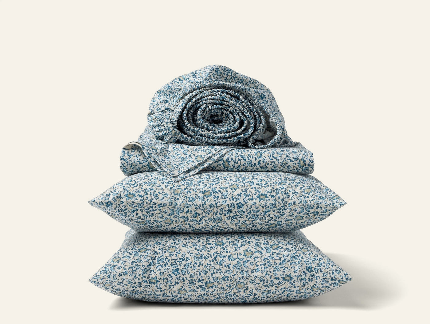 Close-up of stacked Coyuchi Print Percale sheet set in blue floral pattern with rolled duvet on top.
