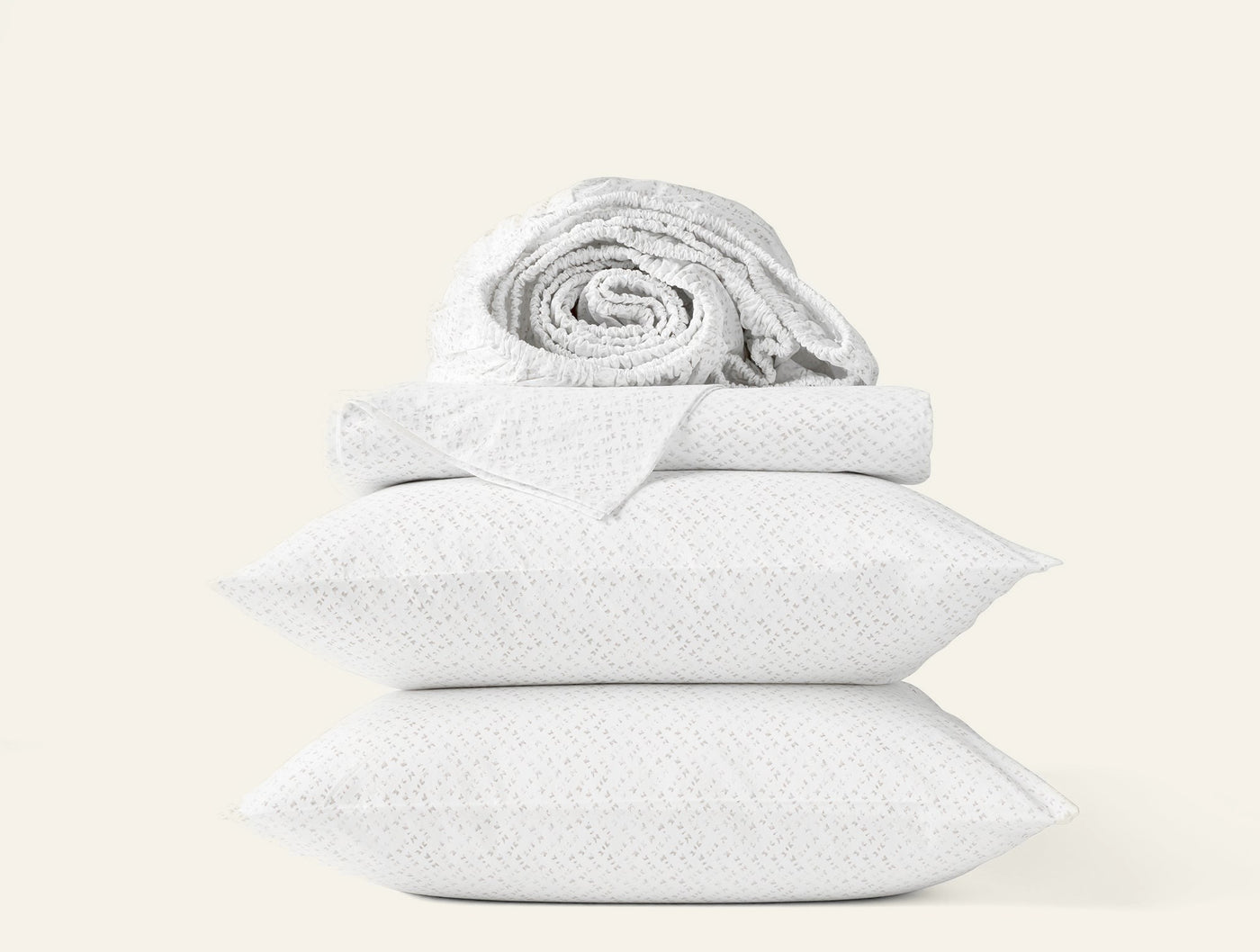 Rolled sheet atop folded pillowcases in white chevron percale, stacked against light background.