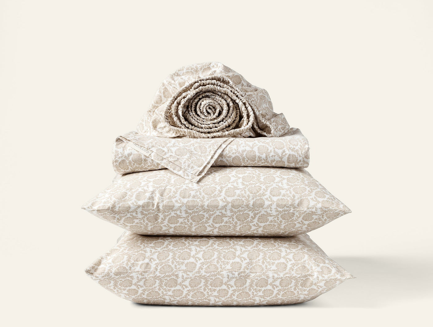Close-up of stacked Coyuchi Print Percale sheet set in taupe geometric pattern, rolled sheet on top.