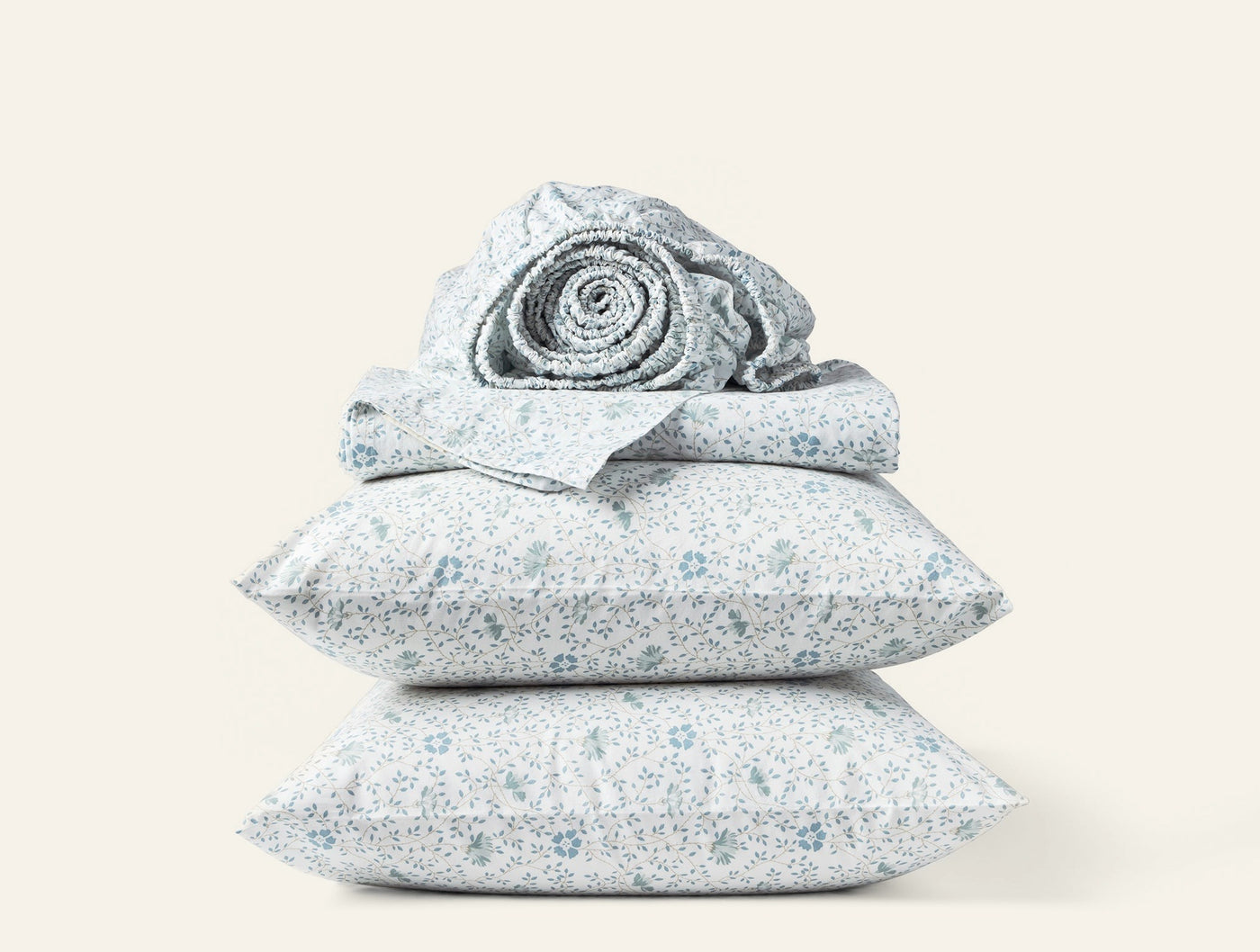Stacked Coyuchi percale pillowcases and rolled sheet in blue floral print on white.