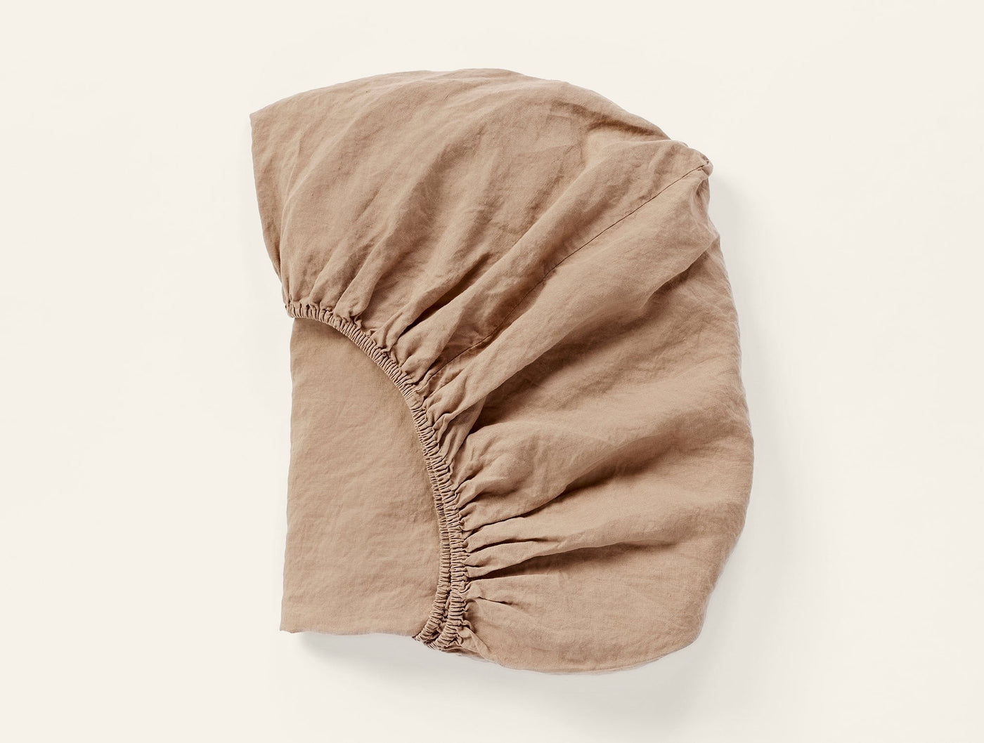 Coyuchi Relaxed Linen fitted sheet in tan, shown flat with elasticated corners visible.
