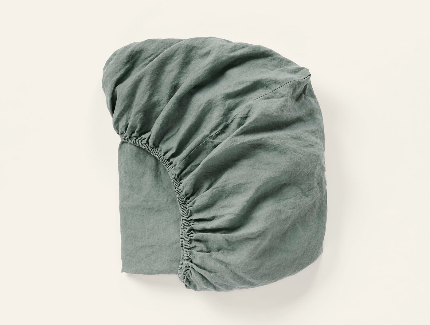 Sage green linen fitted sheet folded to show elasticated corners and relaxed texture.