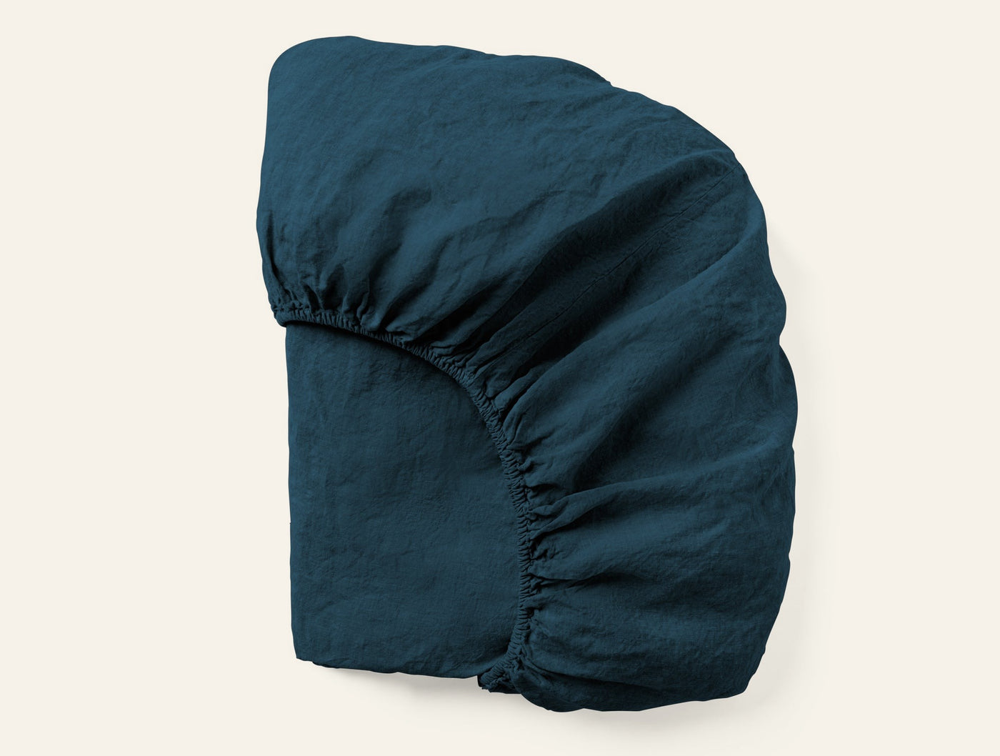 Coyuchi Relaxed Linen fitted sheet in deep teal, folded to show elasticised corners.