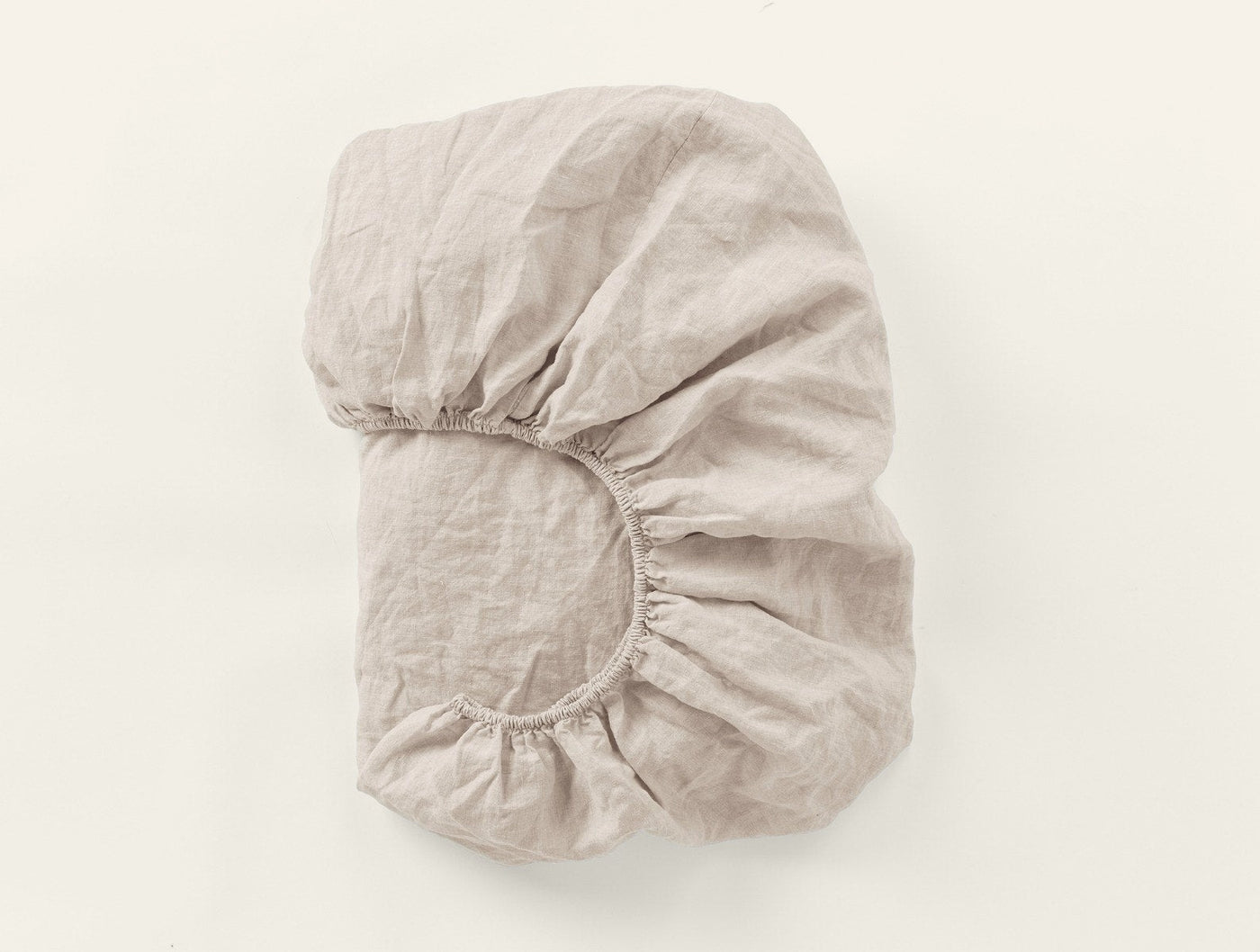Fitted sheet folded to show elastic corner detail, natural linen, relaxed texture.