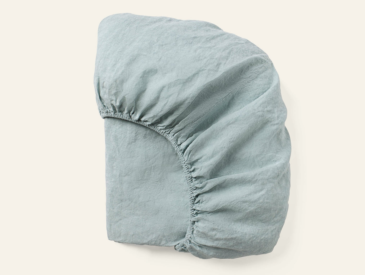Sage green fitted sheet folded to show elasticized corner and relaxed linen texture.