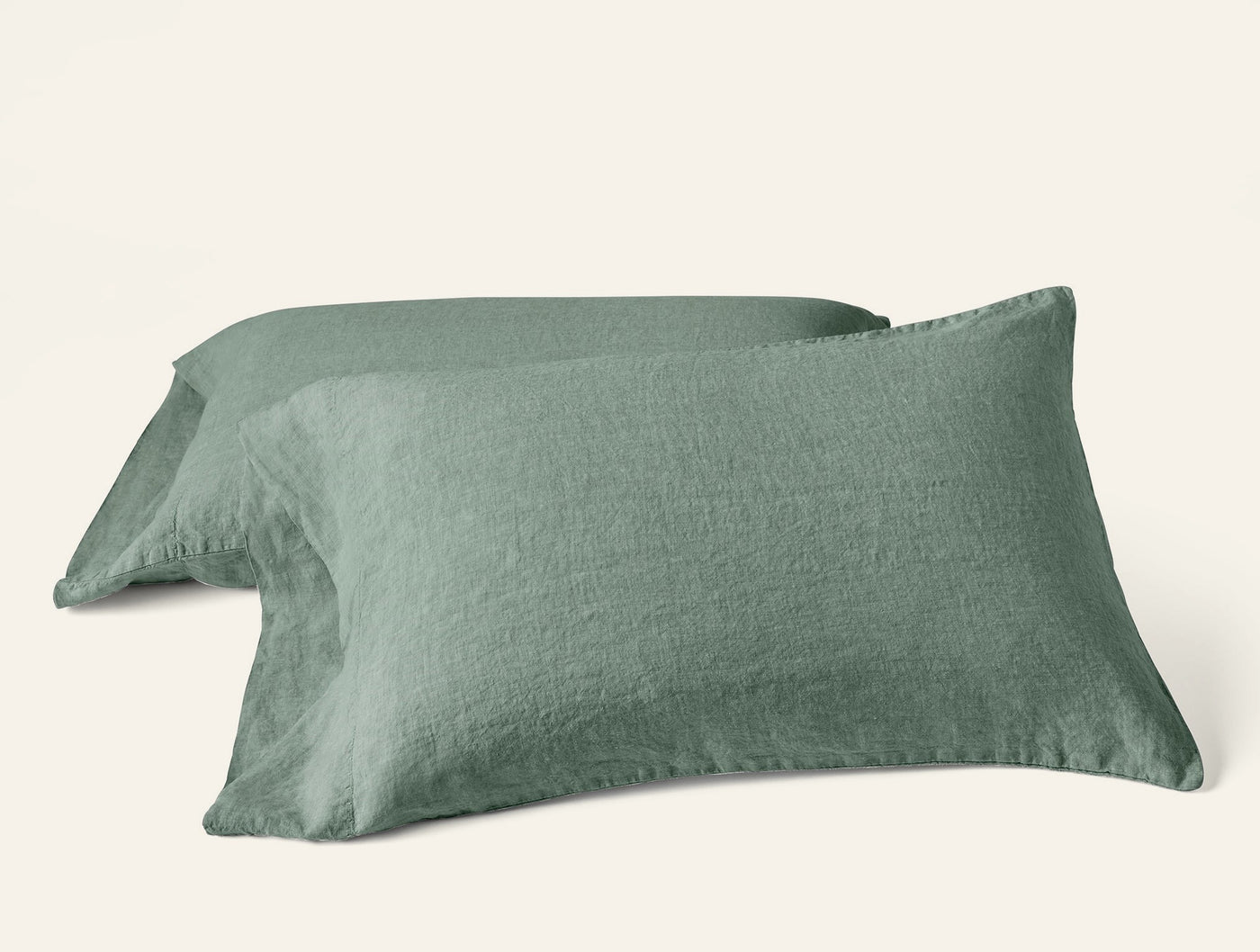 Close-up of two sage Coyuchi Relaxed Linen pillowcases stacked, showing natural texture.