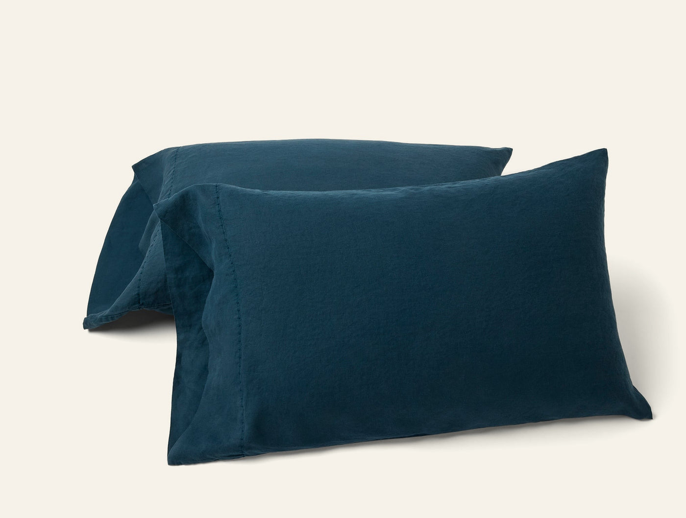 Close-up of two Coyuchi Relaxed Linen pillowcases in deep teal, stacked on white background.