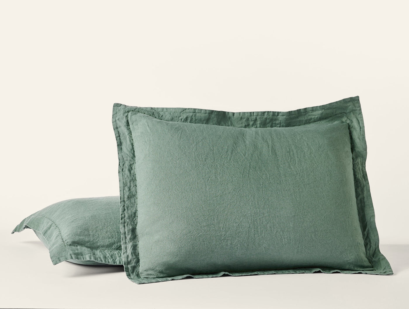 Close-up of two sage green Coyuchi Relaxed Linen pillow shams with flanged edges.