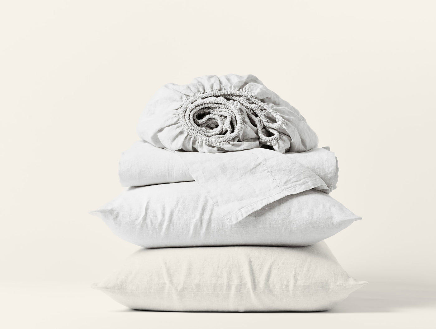 Coyuchi Relaxed Linen sheet set in white, folded stack with pillowcases and rolled fitted sheet.