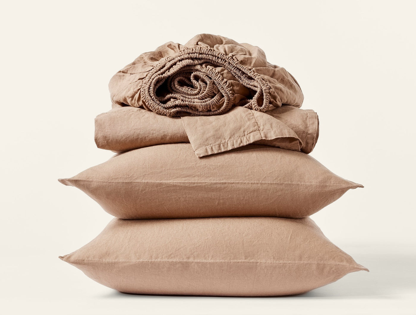 Stacked sand linen pillowcases and folded fitted sheet in relaxed, rumpled texture.