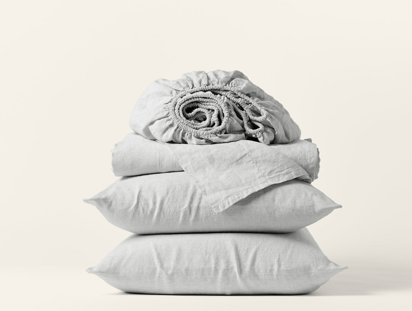 Rolled fitted sheet atop folded flat sheet and two stacked pillowcases in silver grey linen.