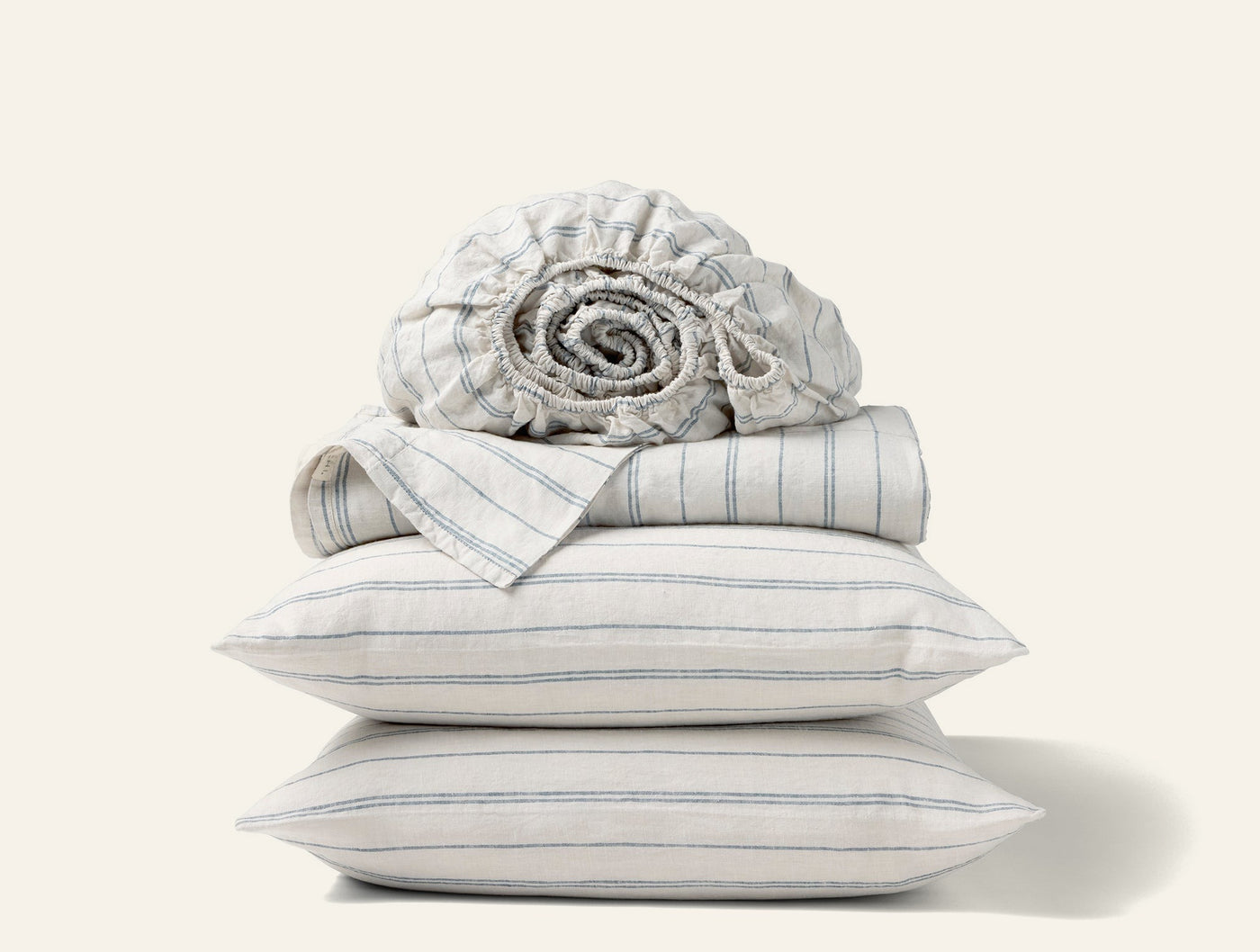 Stacked ivory linen sheet set with blue ticking stripes, rolled fitted sheet on top.