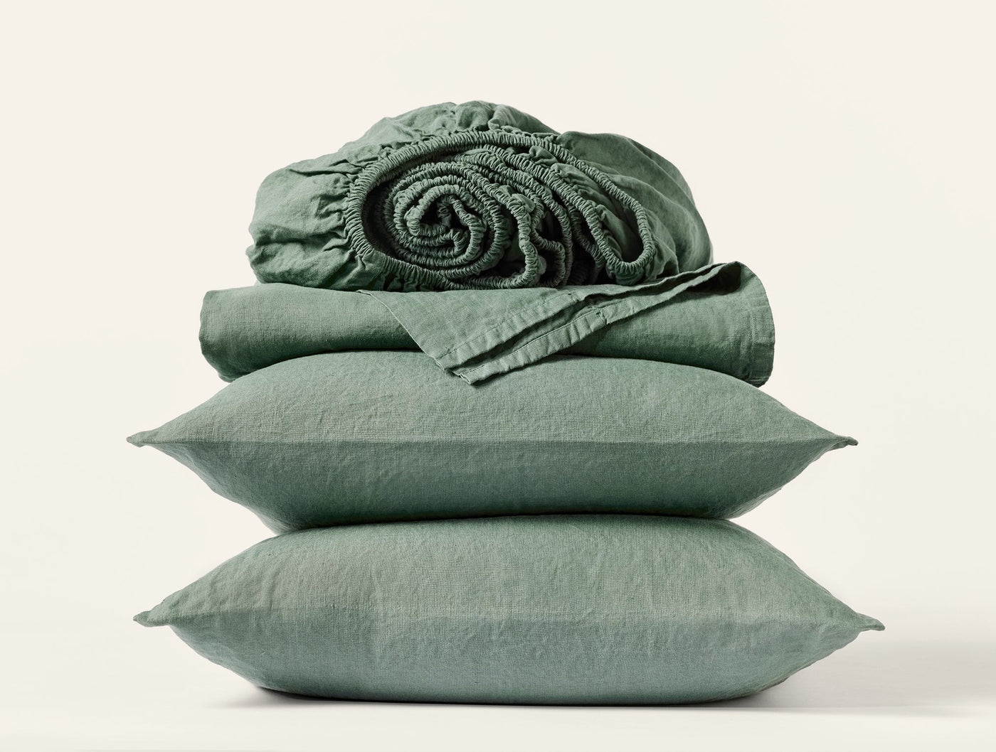 Sage green linen sheet set stacked with pillowcases and rolled fitted sheet.