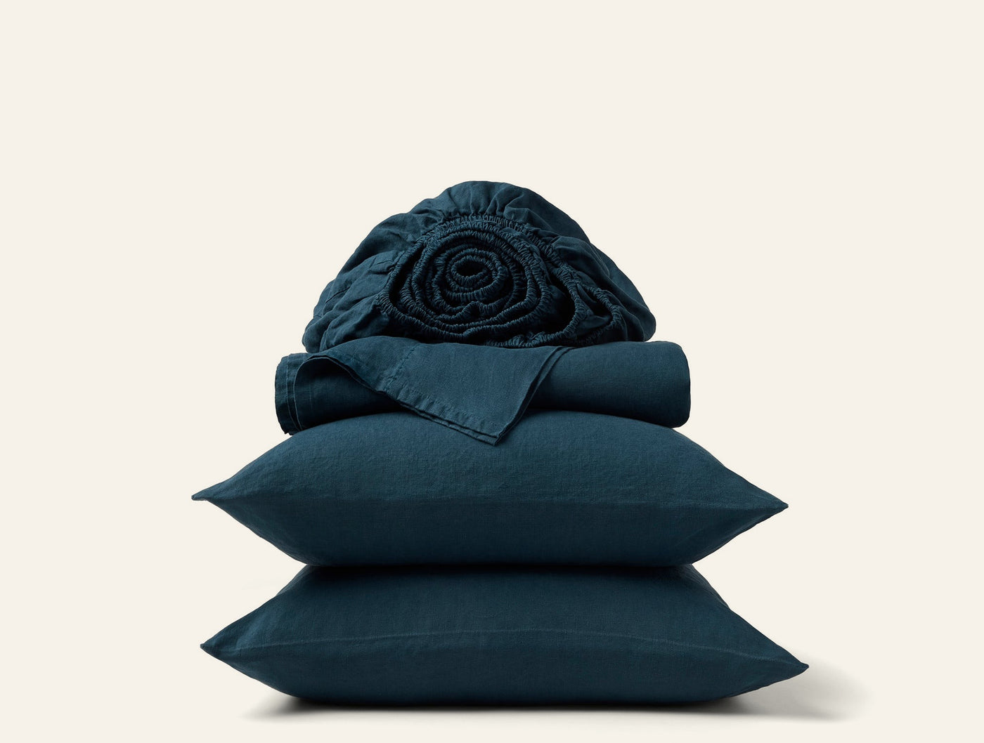 Stacked teal linen pillowcases and sheets with a loosely rolled fitted sheet on top.
