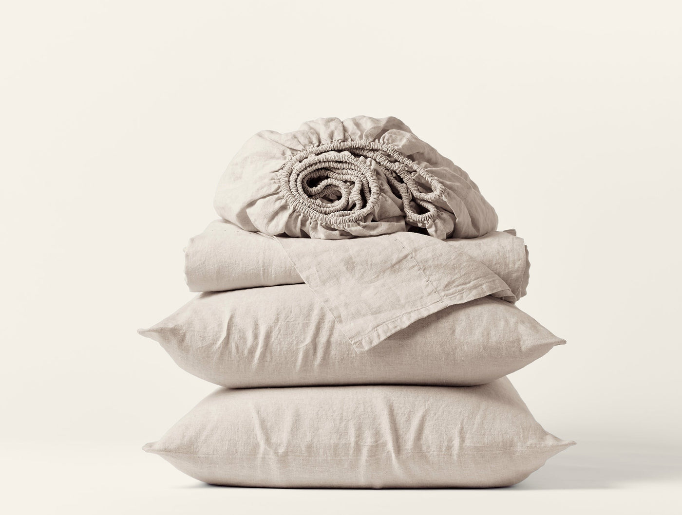 Close-up of stacked natural linen sheet set with pillowcases and rolled fitted sheet.