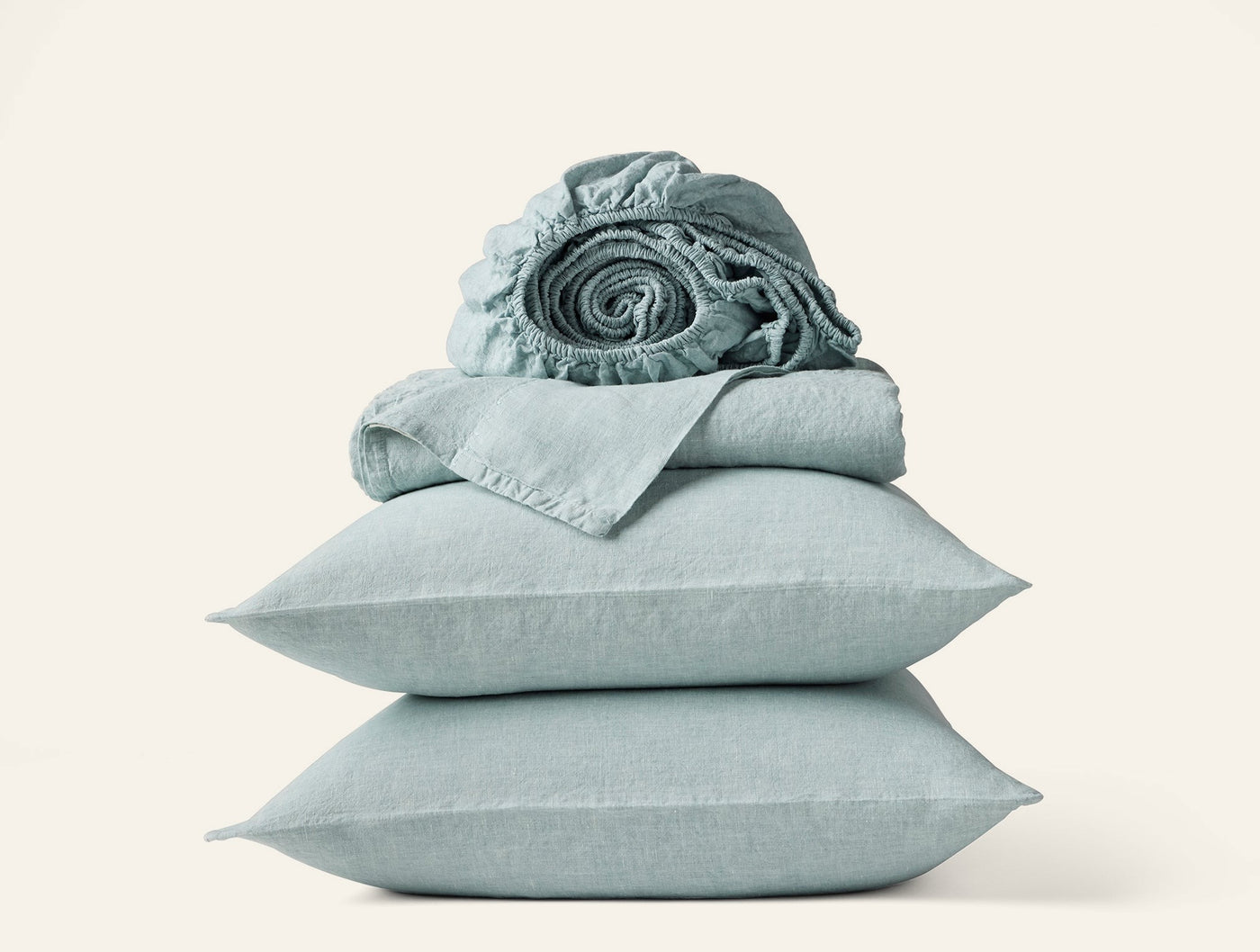Coyuchi Relaxed Linen sheet set in sage, pillowcases stacked with rolled fitted sheet on top.