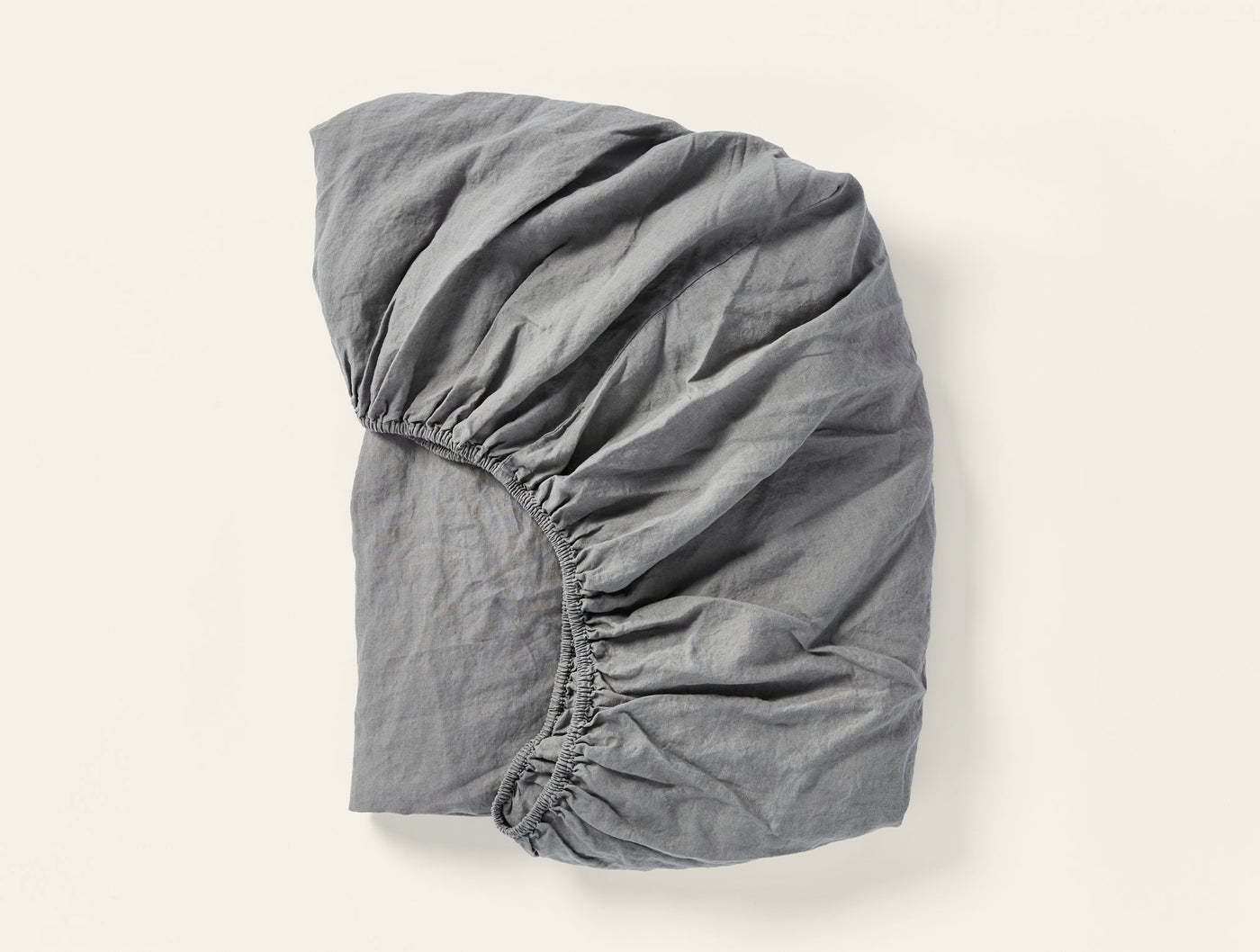 Charcoal linen fitted sheet with visible elastic edge, folded and gathered on white background.