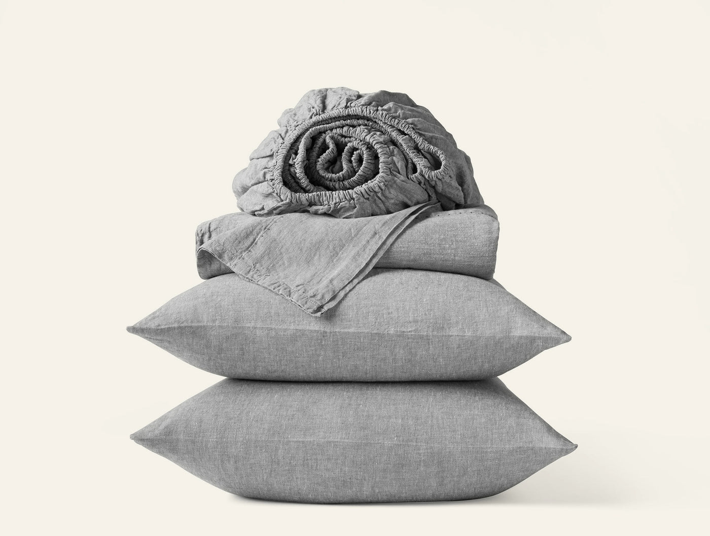 Stacked grey linen sheet set with two pillowcases and a rolled fitted sheet on top.